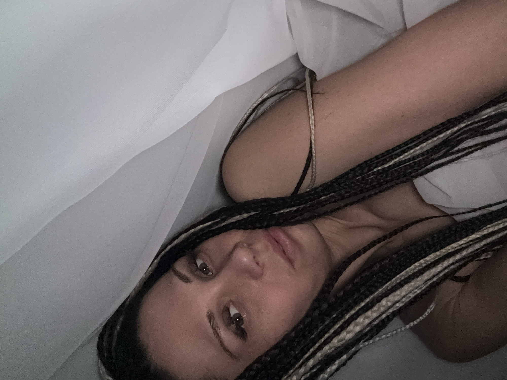 A woman with braided hair is lying down indoors, seemingly under a white sheet or blanket. The environment is dimly lit. The image location, Rusanovo, Russia, cannot be determined from the visual information provided.