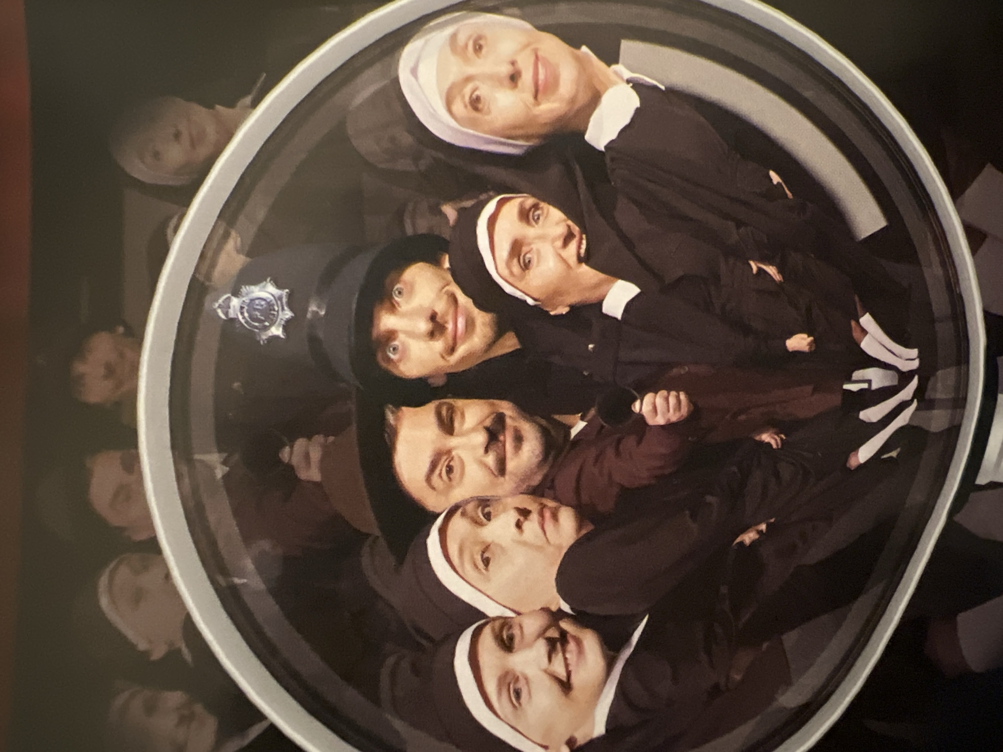 This appears to be a photograph of a reflection in a circular mirror. Within the reflection, there is a group of people. Most of them are dressed as nuns in dark habits with white wimples, with the exception of one man wearing a police officer's hat. The style and context suggest this image might be related to the theater or performance art. Due to the visual nature of the evidence, it is impossible to determine the location of Sofia, Bulgaria.