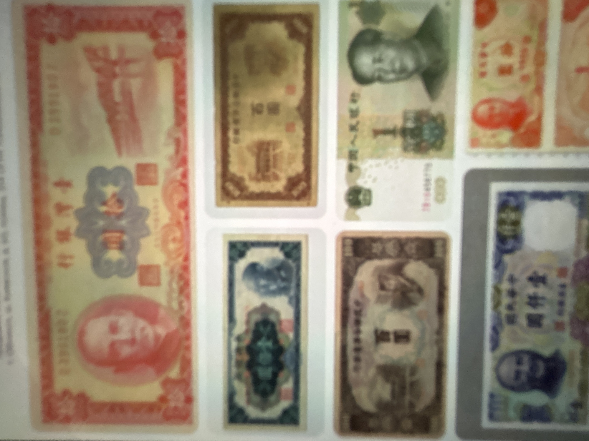 The media file displays a collection of Chinese banknotes laid out on a white surface. The banknotes vary in color, size, and design, suggesting they represent different denominations and possibly different historical periods.
The subjects on the banknotes primarily consist of portraits of people, predominantly male figures with East Asian features. One prominent banknote on the left features a portrait of a person in a circular frame, with Chinese characters above and a number series below. Other banknotes show different individuals, including what appears to be Mao Zedong on one of them. There are also intricate designs and symbols on the banknotes, such as what seems to be a dragon or mythical creature on one and floral patterns on others.
The scene is a still-life arrangement of currency, with no discernible activity or event taking place beyond the presentation of the items themselves. The setting appears to be indoors, on a flat, white surface, possibly a table or a display board. There are no indications of time of day or weather. The location context provided is Gelendzhik, Russia, which is external information and not directly discernible from the image itself.
Notable details include the variety in the banknotes' designs. Some are rectangular and elongated, while others are shorter and wider. The colors range from pale yellow and red to gold and blue. Visible text is in Chinese characters, appearing as denominations, inscriptions, and serial numbers. For example, on one banknote, the characters "壹圆" (one yuan) are visible, and on another, "第五套" (fifth set) and "人民银行" (People's Bank) are discernible. The overall impression is that of a curated collection of currency.