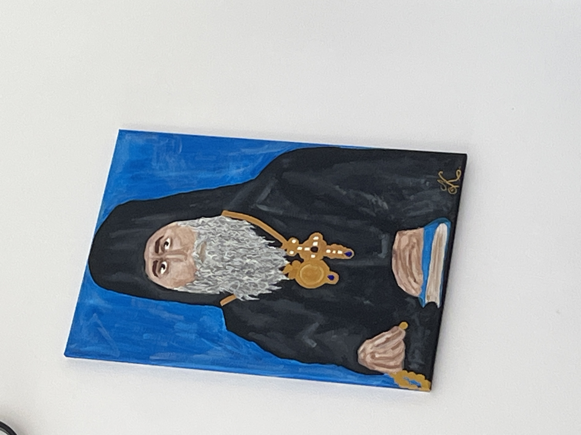 A painting is depicted on a white background. The painting portrays a bearded man wearing black robes and a religious pendant. He holds a book in one hand and prayer beads in the other. The background of the painting is blue. There is no evidence to suggest that this image relates to Zlatograd, Bulgaria.