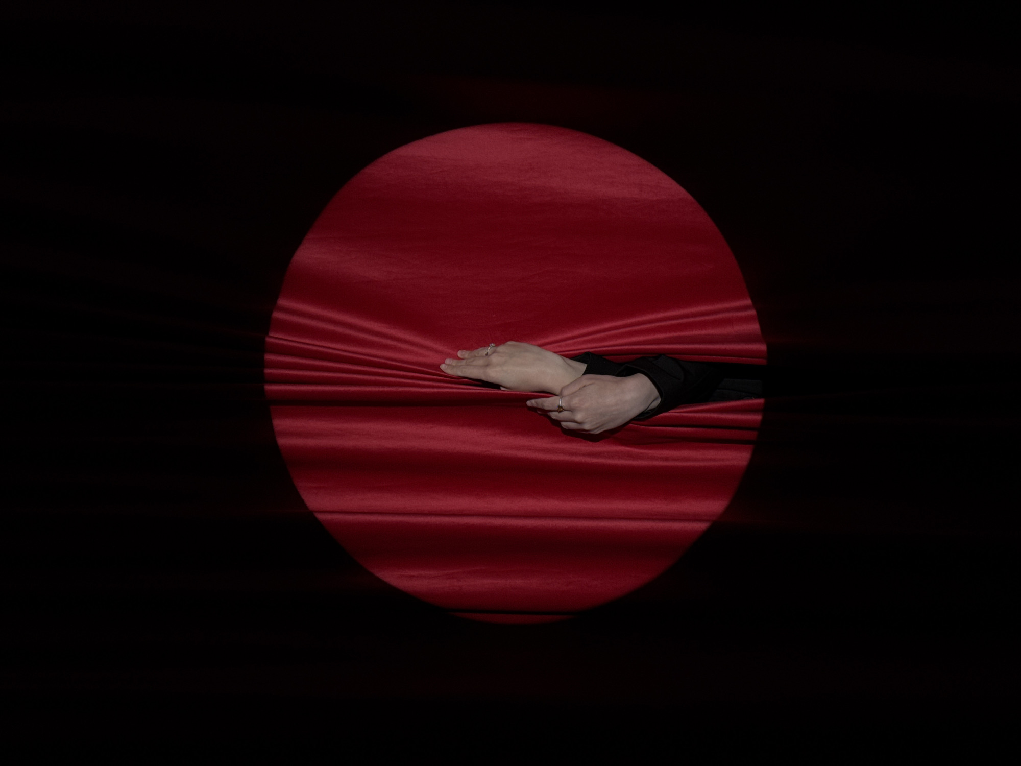 A circular area of red velvet is illuminated against a black background. A pair of hands wearing rings emerge from the velvet. The location of the city of Chaikovsky, Russia is not evident in the image.