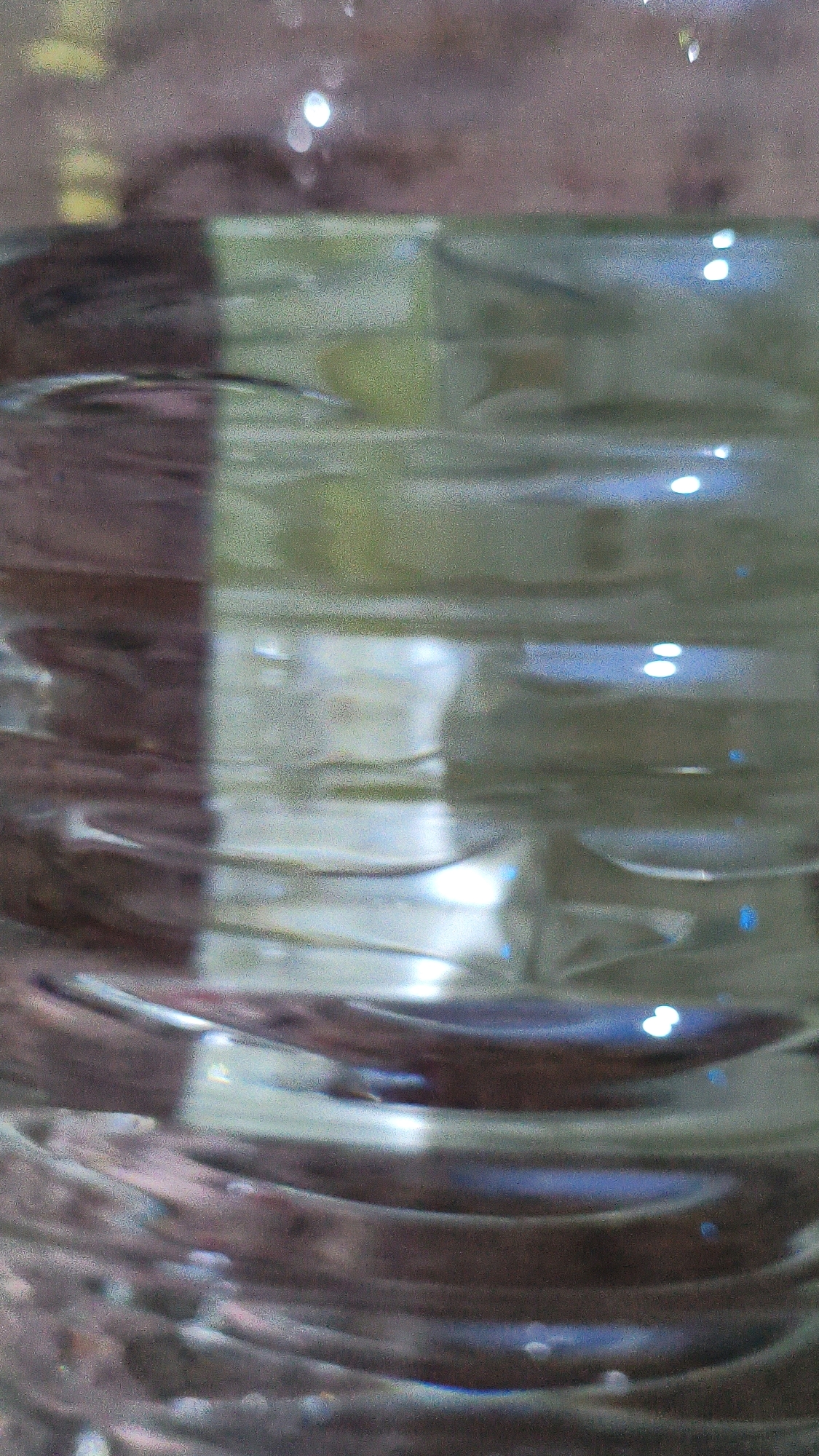 The image displays a close-up, abstract view of what appears to be a textured surface, possibly a bottle or a cylindrical object, with varying light reflections. There are no discernible elements that would allow for a description of a location in Mehnatabad, Uzbekistan, or any specific people, actions, or interactions. The scene is devoid of any recognizable urban or natural environment features.