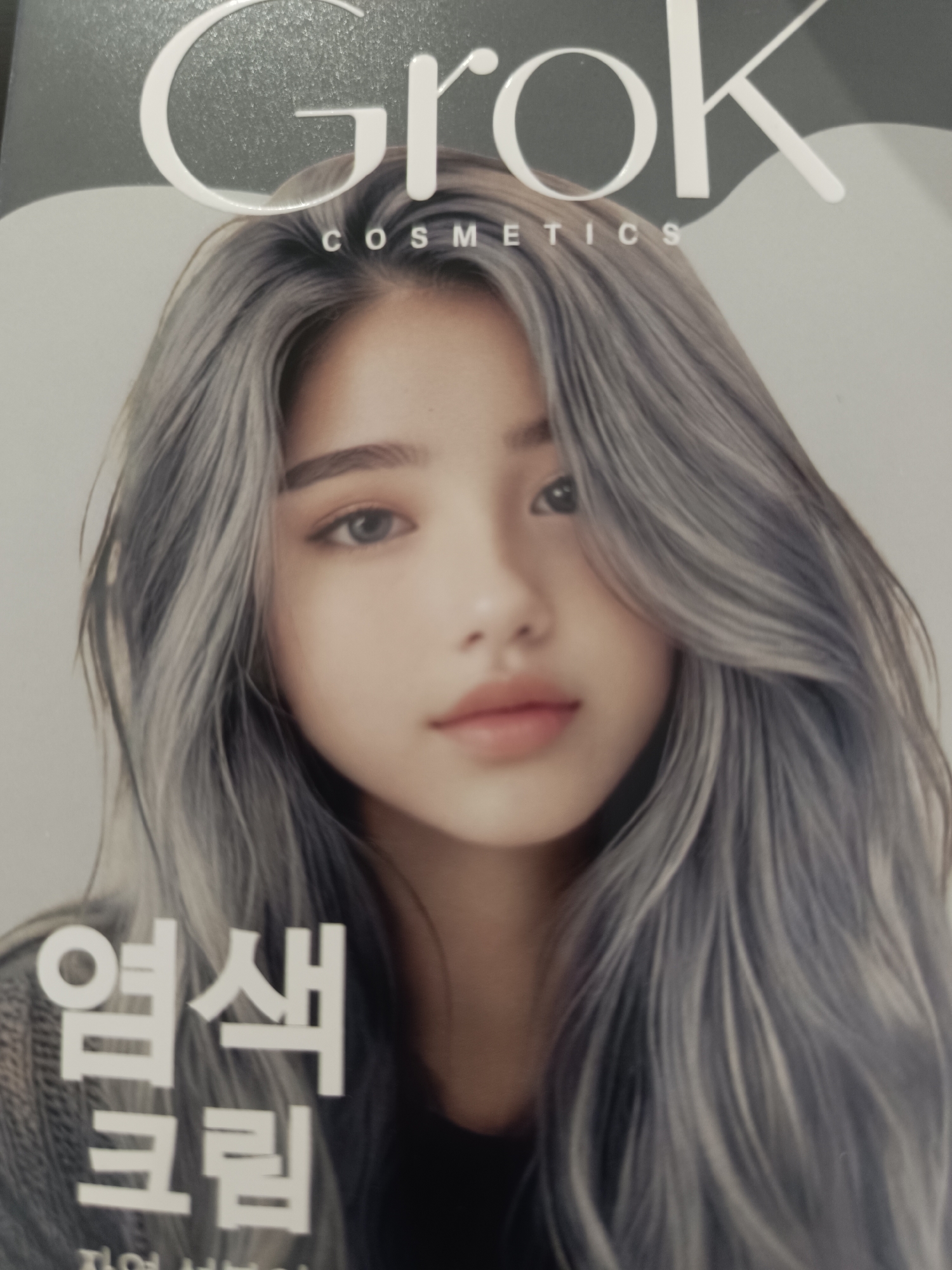 The cover of a magazine or product features a close-up of a young woman with long, wavy, ash-blonde hair. Her face is turned slightly towards the viewer, with her gaze directed forward. She has striking, light-colored eyes and full lips. The woman is wearing a dark, textured garment, possibly a sweater. The background is a soft, neutral gray, with a subtle curve in the upper left corner that suggests a studio or staged setting.
Prominently displayed at the top of the cover is the word "Grok" in large, stylized white lettering. Below it, in smaller white text, are the words "COSMETICS".
In the lower left portion of the cover, there are two lines of text in Korean. The first line, in large, bold white characters, reads "염색" (yeomsaek), meaning "hair dye" or "coloring." The second line, also in white characters, reads "크림" (keurim), meaning "cream." This suggests the product being advertised is a hair coloring cream.
The overall mood is elegant and sophisticated, with the focus on the woman's beauty and the product's branding. There are no specific time of day or weather cues, and the location is implied to be a commercial setting for product advertisement. The woman's expression is neutral, conveying a sense of serene confidence.