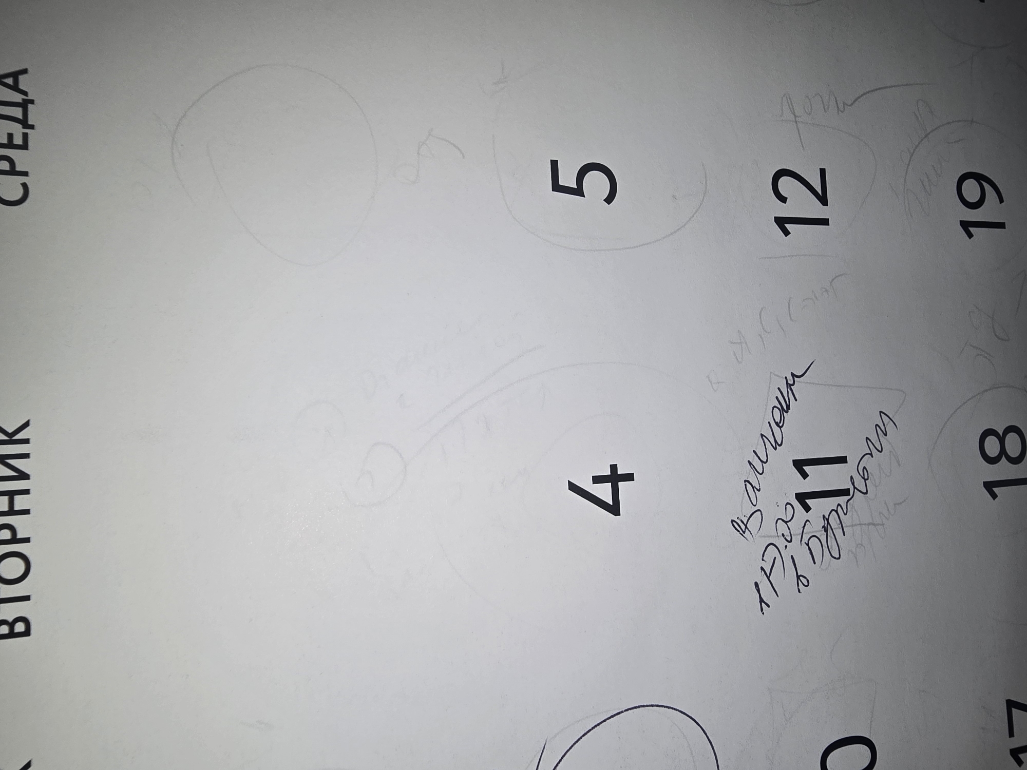 The image is a close-up of a calendar page. The calendar is written in Cyrillic. At the top of the page, the words "ВТОРНИК" (Tuesday) and "СРЕДА" (Wednesday) are visible. Below these headings, several numbers are printed, representing dates. The visible dates are 4, 5, 11, 12, 18, and 19. There are also handwritten annotations on the calendar. Specifically, around the number 11, there are scribbled notes in Cyrillic, including what appears to be a time, "17:00", and other illegible text. There are also faint circular drawings and scribbles across the page, indicating use and possibly doodling. The background is a textured, light-colored paper. The image does not contain any information or visual cues that would allow for identification of its location in the city of Ulan-Ude, Russia.