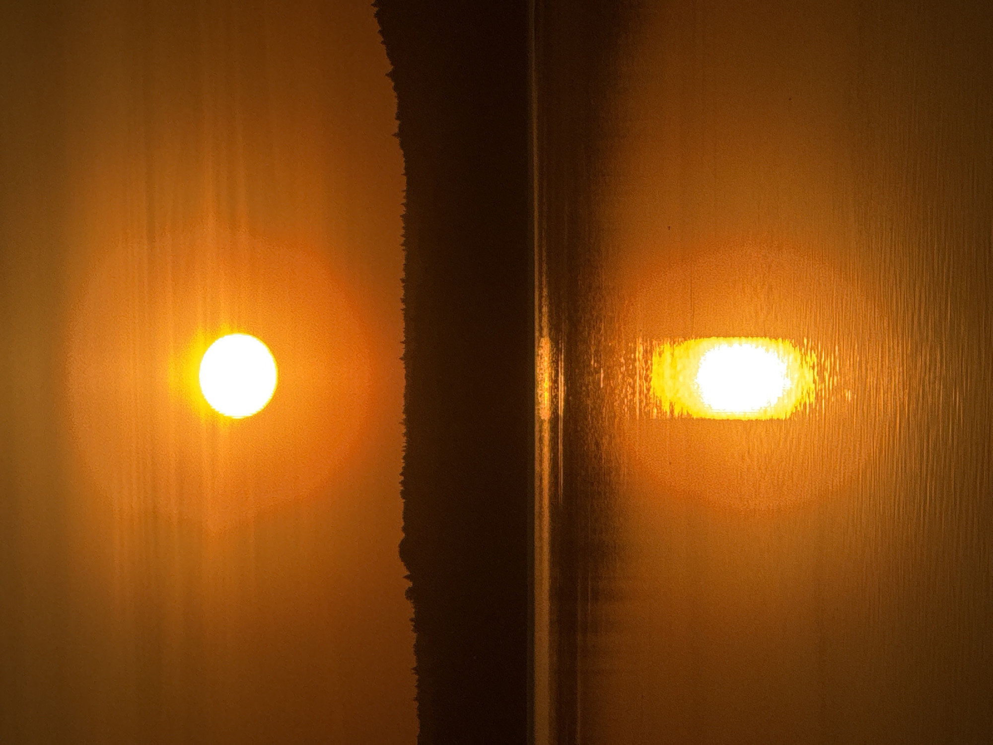 The image shows two bright light sources, possibly suns or reflections, on two textured surfaces separated by a dark vertical line. The surface on the left appears rougher, while the right surface exhibits vertical striations. The overall color is a warm orange, suggesting a sunset or artificial lighting. The location of this scene cannot be determined to be in Votkinsk, Russia, without additional information.