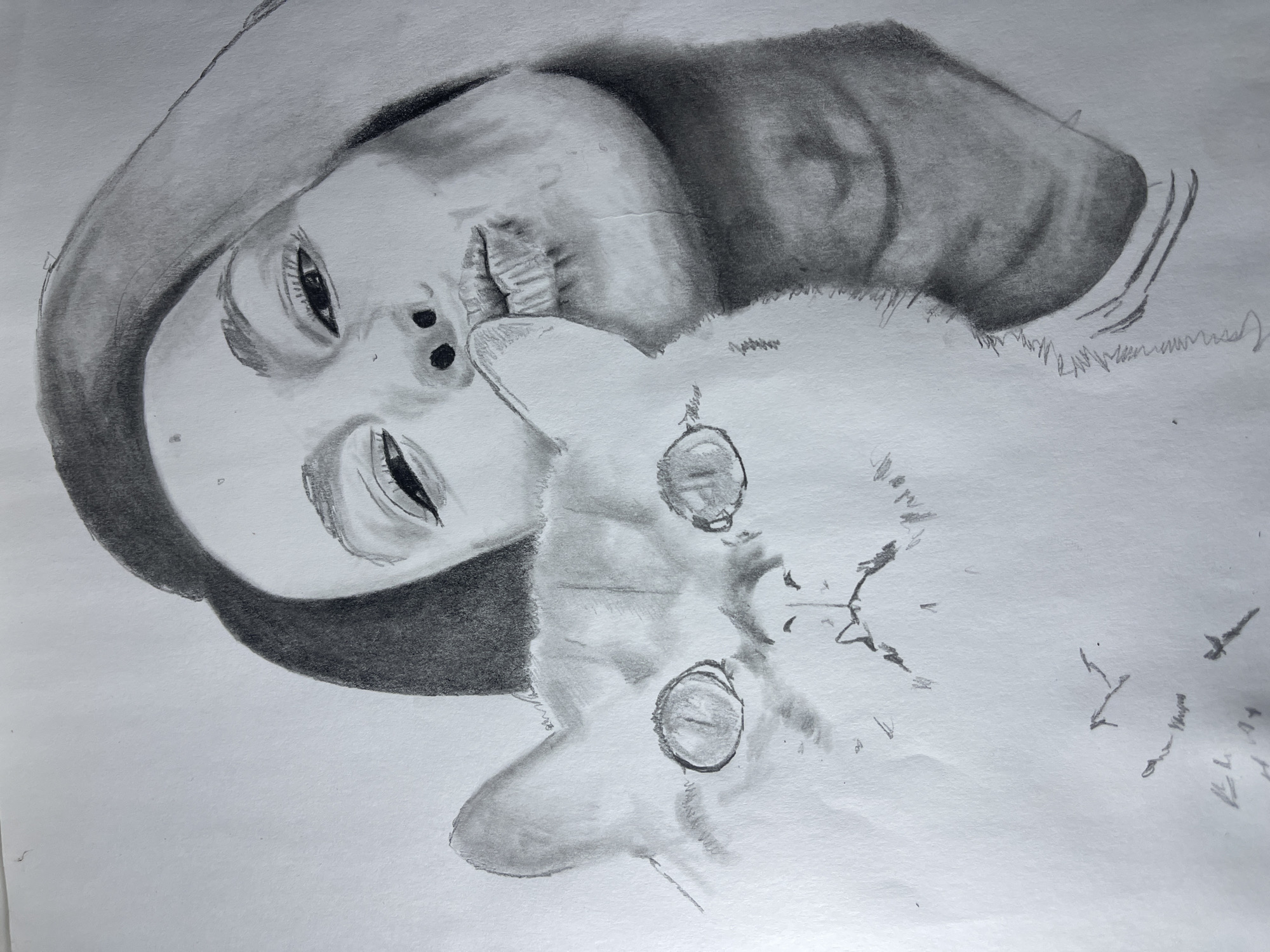 This image is a black and white pencil drawing on white paper, depicting a woman embracing a cat. The drawing is oriented vertically.
**Subjects:**
A woman occupies the upper right portion of the drawing. Her face is presented in profile, tilted, with her eyes mostly closed and her lips pursed in a kissing gesture, directed towards the left. Her hair, rendered in dark shading, frames her head and extends to the right. Facial features such as eyebrows, eyelashes, and a small nose are visible.
A domestic cat is positioned to the lower left, overlapping the lower part of the woman's face and chest area. The cat's head is in a front-facing or slightly upward-looking pose. It features large, circular, dark-shaded eyes, a small triangular nose, and an open mouth with visible teeth. Its left ear is partially visible above its head. The cat's fur is depicted with lighter shading, contrasting with the woman's hair.
**Action and Interaction:**
The woman's puckered lips are in close proximity to the cat's head, suggesting an affectionate interaction, specifically a kiss or an attempt to kiss the cat. The cat's expression is neutral to slightly startled or attentive.
**Environment:**
The environment is a white paper surface. The drawing itself is rendered with graphite, showing varying shades from light grey to dark charcoal. There are minimal smudges and faint, erratic pencil marks in the lower-left corner of the paper, outside the main subjects.
The image is a representation of an artwork. The scene depicted within the drawing does not specify or indicate any real-world geographical location within the city of Jos, Nigeria, or any other physical setting. The "environment" is the artistic medium and surface.