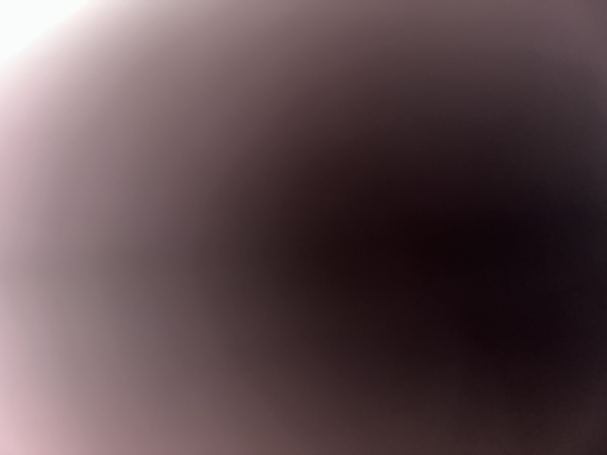 The media file is a photograph with a gradient of light and dark tones, shifting from a pale pinkish-white in the top left corner to a deep, dark brown in the bottom right. There are no discernible subjects, objects, scene, or setting. The activity or event taking place is unclear, and there are no notable details such as time of day, weather, location cues, or emotions. No text is visible in the image. The provided crops do not reveal any additional information. The image appears to be abstract or a result of a photographic anomaly, possibly lens flare or an out-of-focus shot.
