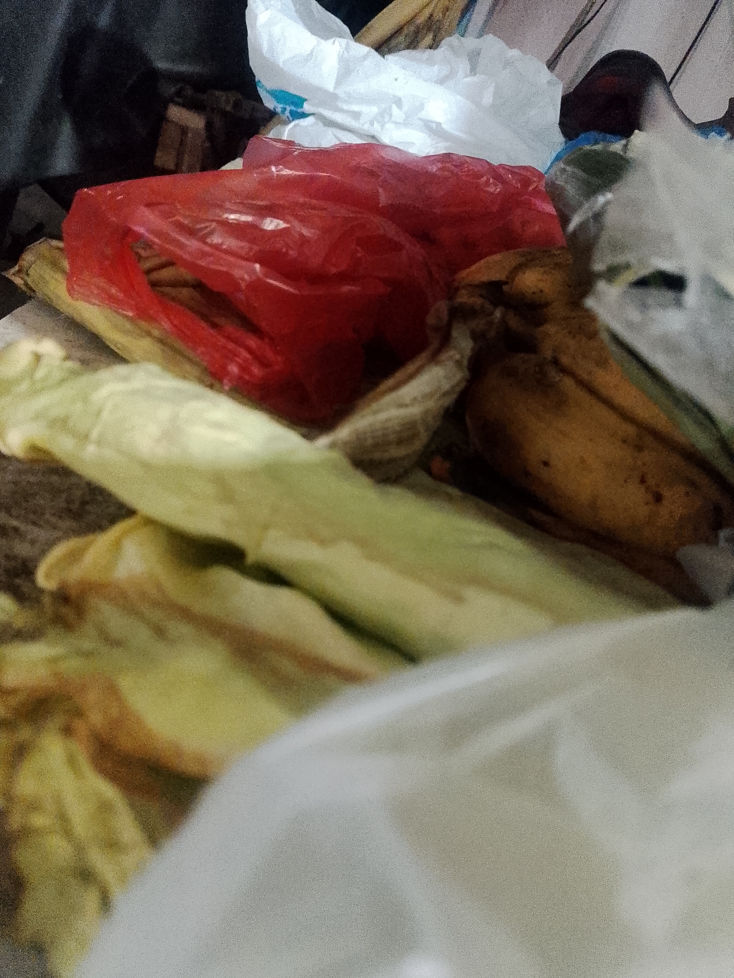 The image shows a pile of trash. The trash includes corn husks, a red plastic bag, a white plastic bag, and other unidentified waste. The exact location in Lhokseumawe, Indonesia, is not discernible from the visual information.