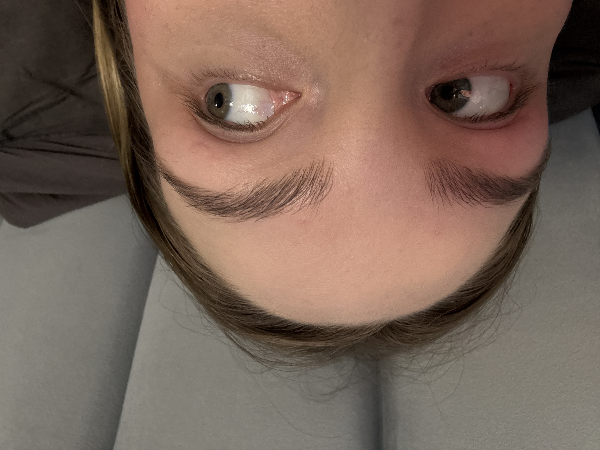 A close-up, slightly skewed photograph depicts a person's face, specifically from the forehead to the eyes and eyebrows. The person's eyes are looking upwards and towards opposite sides. The hair is light brown and touches the forehead. The skin tone is fair. The background appears to be a textured light gray surface. There is no information to determine the location or connection to Chaikovsky, Russia.