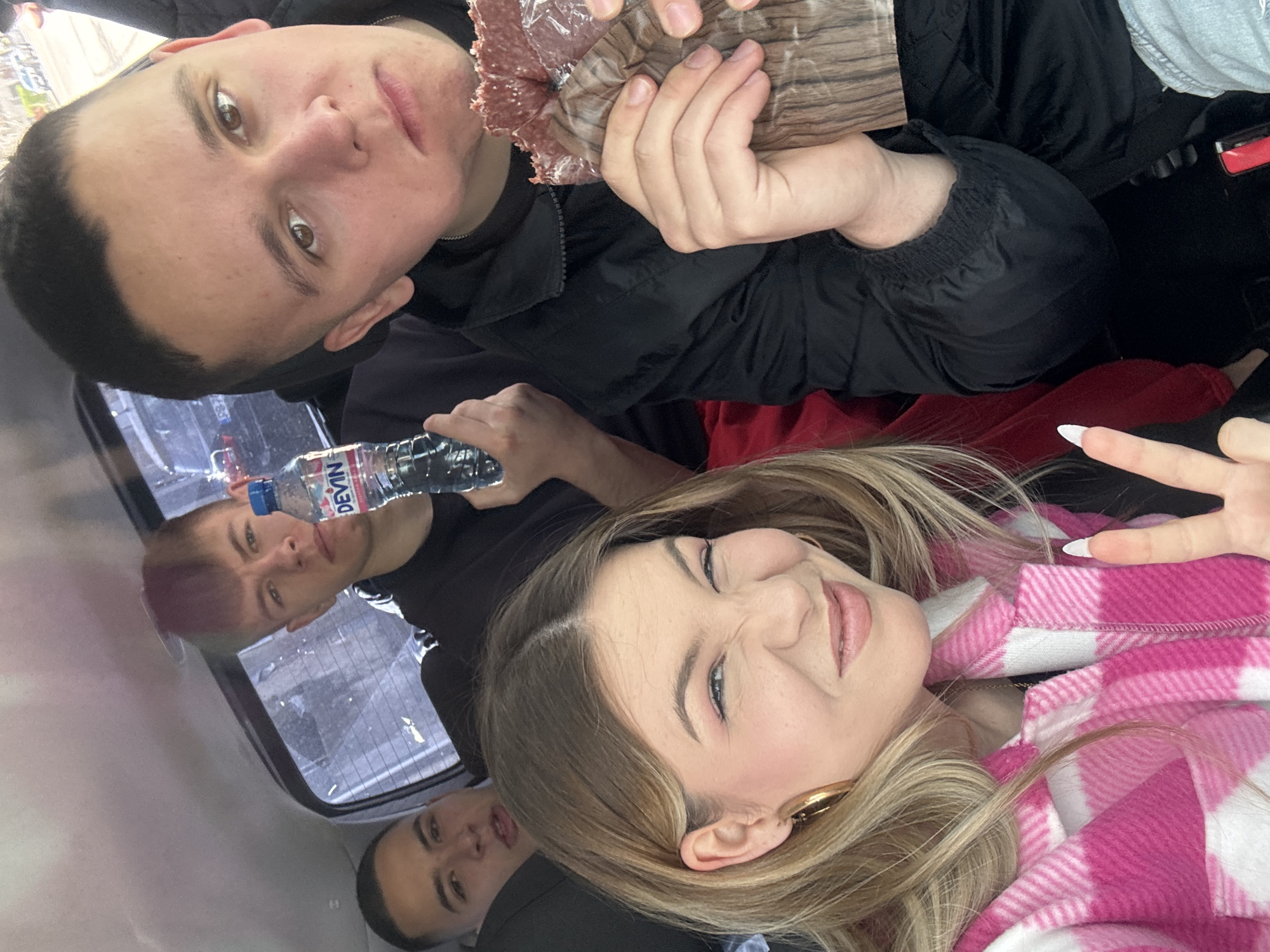 Four individuals are present in an enclosed space, presumably a vehicle. One individual at the top of the frame is holding a package of meat. Another individual is holding a water bottle. A female individual is making a peace sign. The location of Parvenets, Bulgaria, is not discernible from the image.
