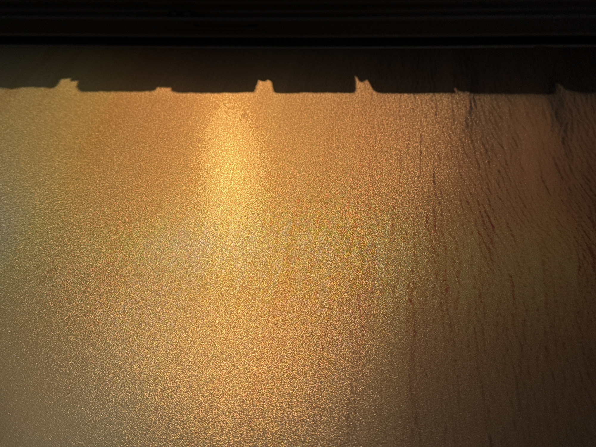 The image shows a frosted window, partially illuminated by golden sunlight. The top of the window is shadowed by a dark frame and what appears to be the edge of a building or overhanging structure, creating an irregular shadow pattern. The frosting on the glass obscures the view outside, giving a textured appearance to the light filtering through. The right side of the window is darker, suggesting a difference in light exposure or the presence of an object casting a shadow.
It is not possible to verify the location of this image in Kladovitsy, Russia, from the provided details.