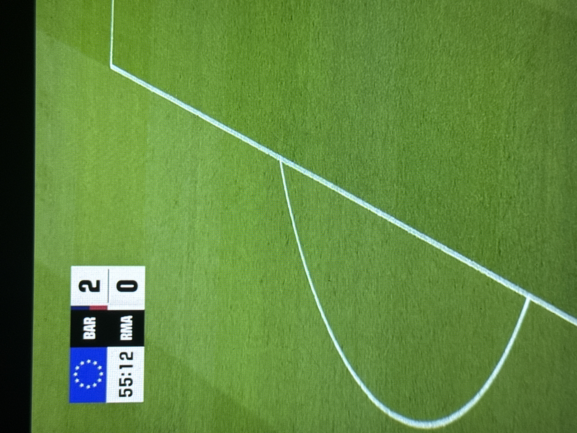 The image shows a green soccer field with white lines marking the penalty area. The scoreboard indicates a match between BAR (Barcelona) and RMA (Real Madrid) with a score of 2-0 at 55:12. The location in Babynino, Russia, is not evident from the image.