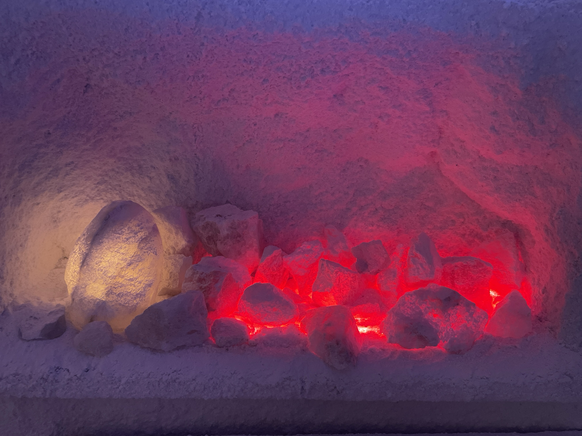 The image depicts a salt room, likely for therapeutic purposes, featuring a recess filled with salt rocks illuminated with red and yellow lights. The walls and the platform beneath the rocks are covered in a layer of fine salt crystals, creating a snow-like texture. The location is suggested to be in the city of Vinnytsia, Ukraine, though no specific identifying details are visible in the image itself.