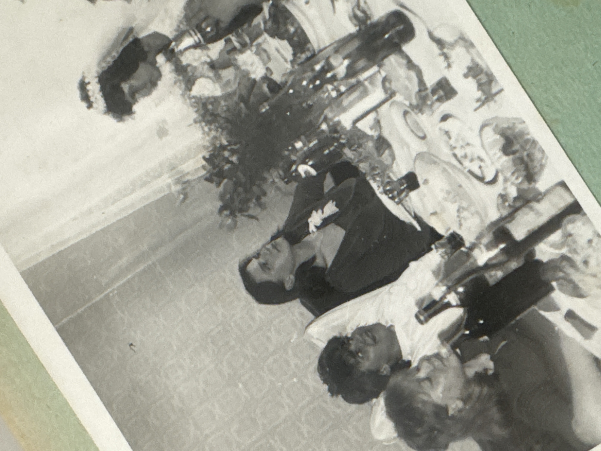 The image is a black and white photograph of a wedding reception. There is a table set with plates, bottles, and flowers. Several people are seated at the table, including a man in a suit and tie and at least two women with dark hair. The location in the city of Ramat Gan, Israel is not evident.