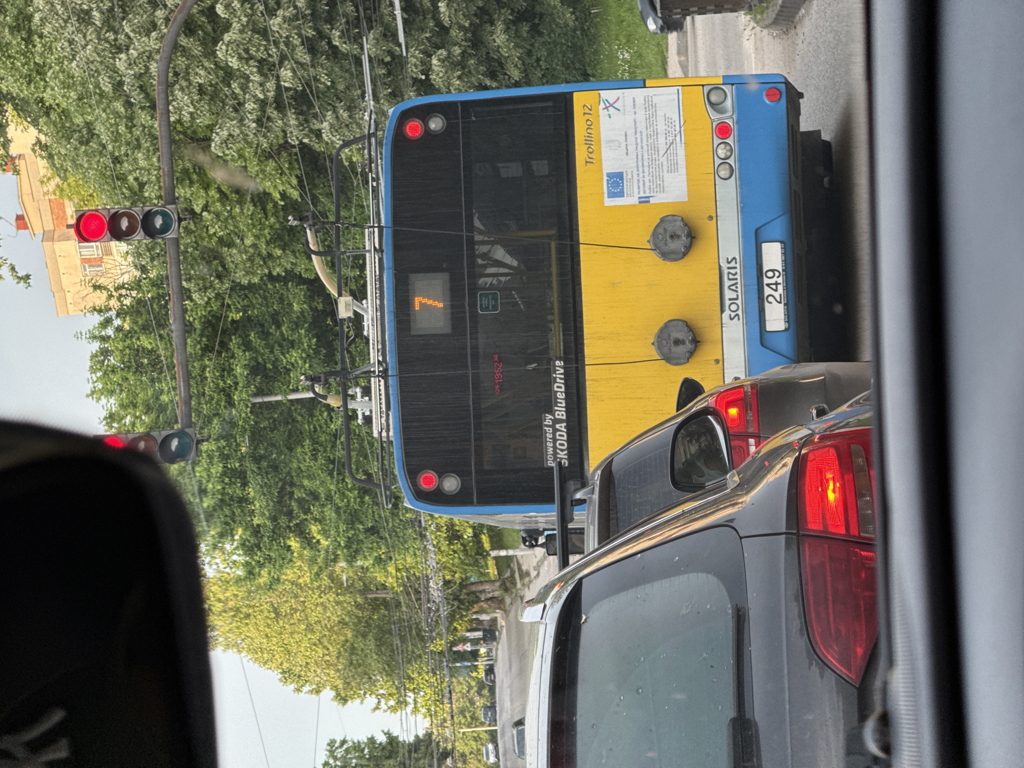 The image, taken from inside a car, shows a Solaris Trollino 12 trolleybus with license plate number 249 at a red traffic light. The trolleybus, numbered 7, is yellow and blue and is powered by SKODA BlueDrive. Other cars are visible. The location is Pleven, Bulgaria, based on the bus livery.