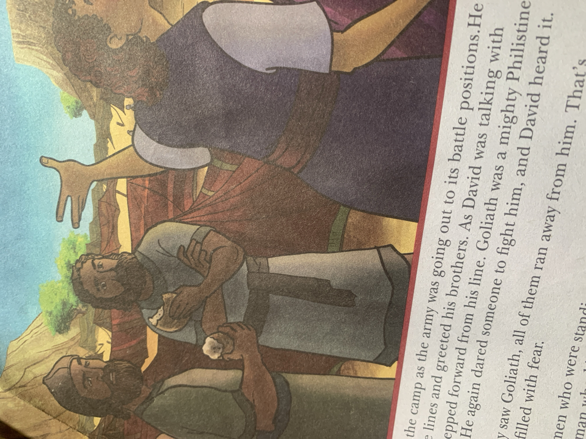 The image shows an illustration from a book depicting three men in an outdoor setting with tents and rocky hills in the background. Two men in the foreground, on the left, are facing forward and appear to be conversing. One is wearing a dark cap and a green tunic, while the other has a gray tunic and is holding a piece of food. A third man is seen from behind on the right, with his arm raised and hand open, as if gesturing or speaking. He wears a dark blue robe with a red sash. The text below the illustration mentions "the camp as the army was going out to its battle positions," and refers to "David" and "Goliath." There is no information in the image or text that suggests a connection to Jauro Yinu, Nigeria.