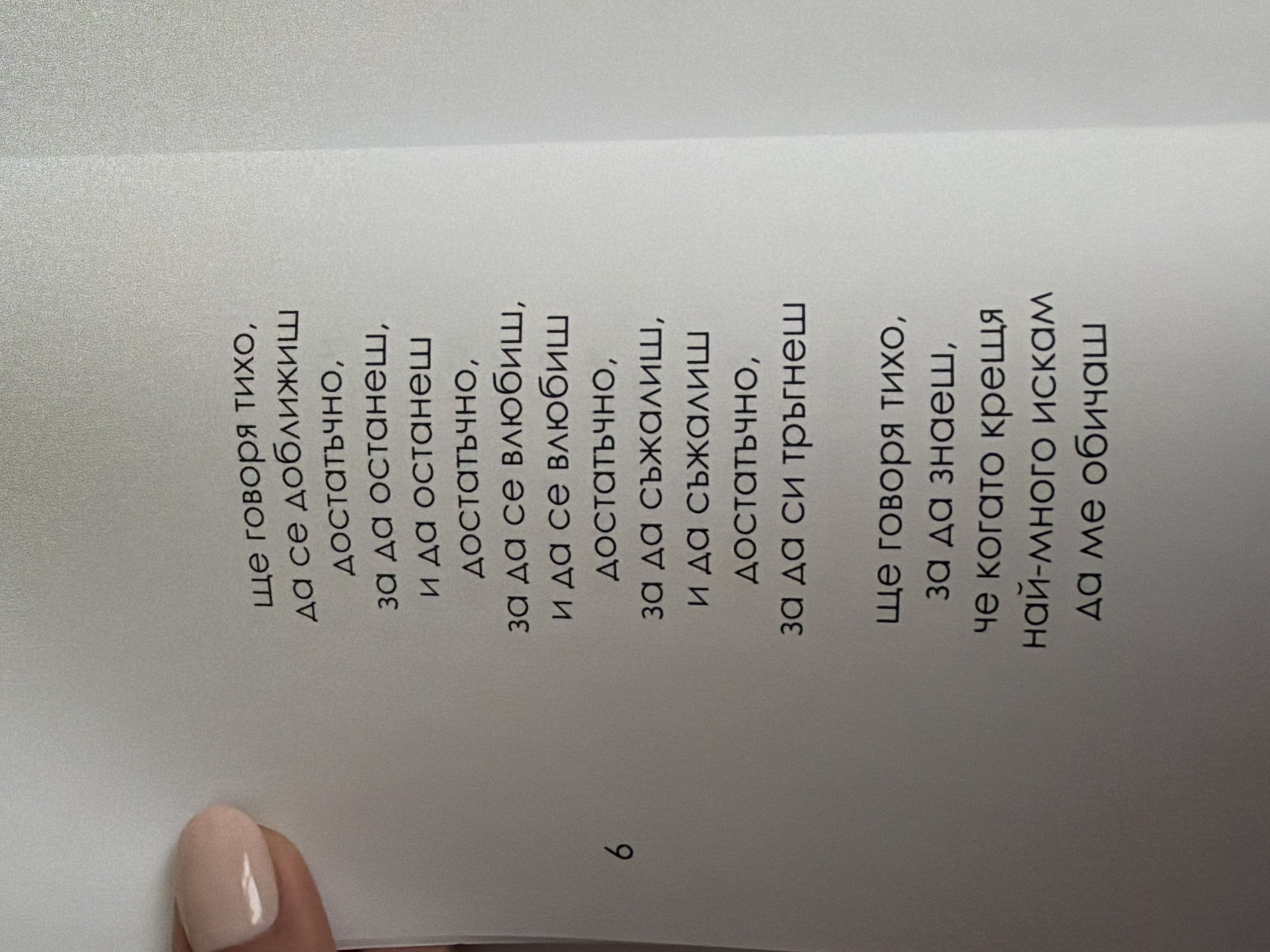 The image shows a page from a book with Bulgarian text. The text is arranged in several stanzas, with the page number "6" visible on the left side. A person's fingernail, painted with light pink polish, is visible in the upper left corner of the image, suggesting the book is being held. The background is a plain, light-colored surface. There is no information in the image to suggest a location in Pazardzhik, Bulgaria.