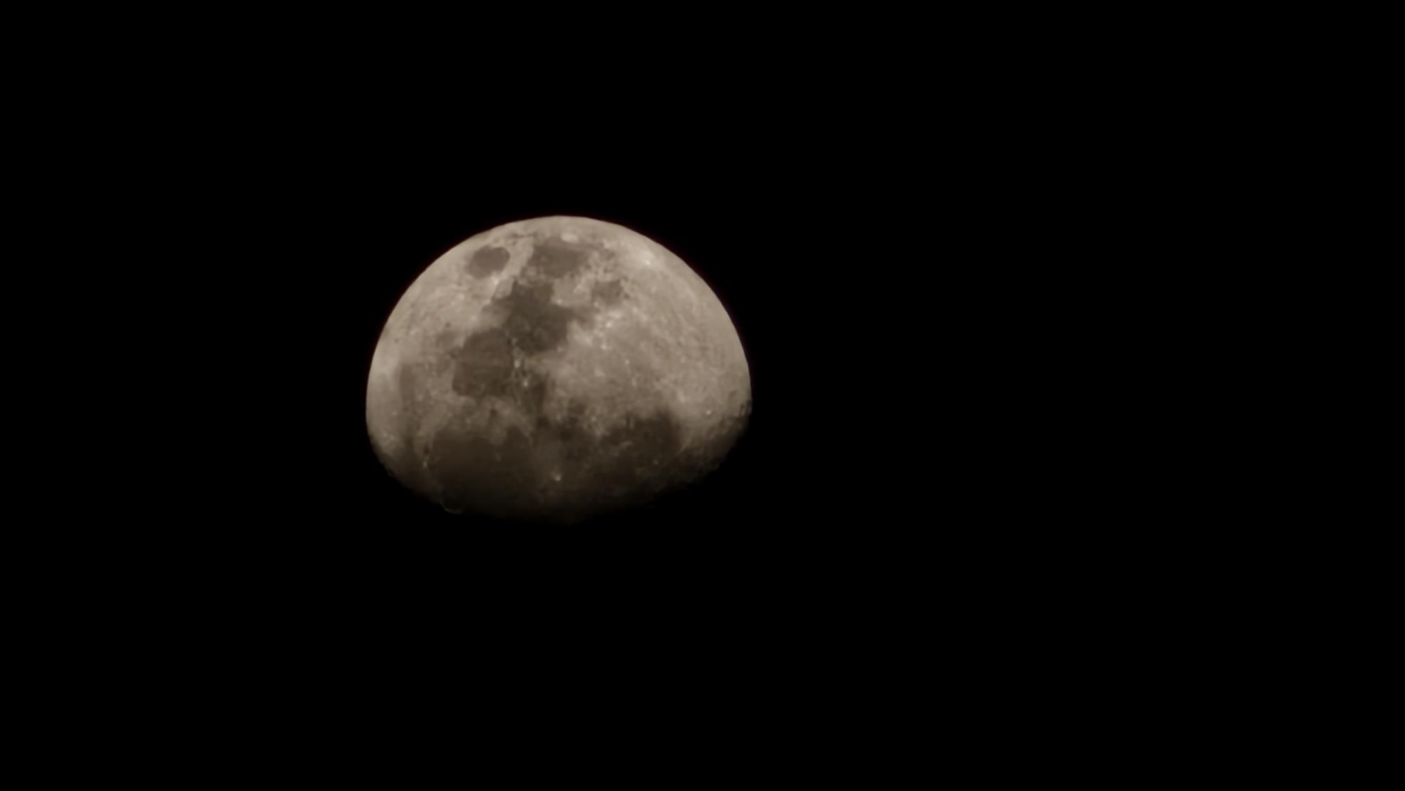 The image is a close-up, vertical shot of the moon against a black sky. The moon is partially illuminated, showing craters and surface details. The lighting suggests it is nighttime. The image does not contain any elements that would allow for the identification of a specific location, such as the city of Krasnodar, Russia. There are no people, objects, actions, interactions, or environmental features present that would indicate a cityscape or geographical context.