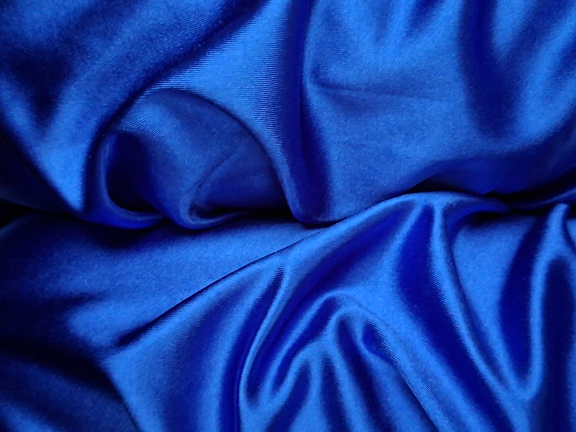 A close-up, overhead shot displays the texture and folds of a vibrant royal blue fabric. The lighting creates strong contrasts, highlighting the sheen and the subtle vertical ribbing of the material. There are no discernible objects, people, or environmental features present in the image, as it is solely focused on the fabric itself. The location in Krilovo, Russia, is not evident from the visual information provided.