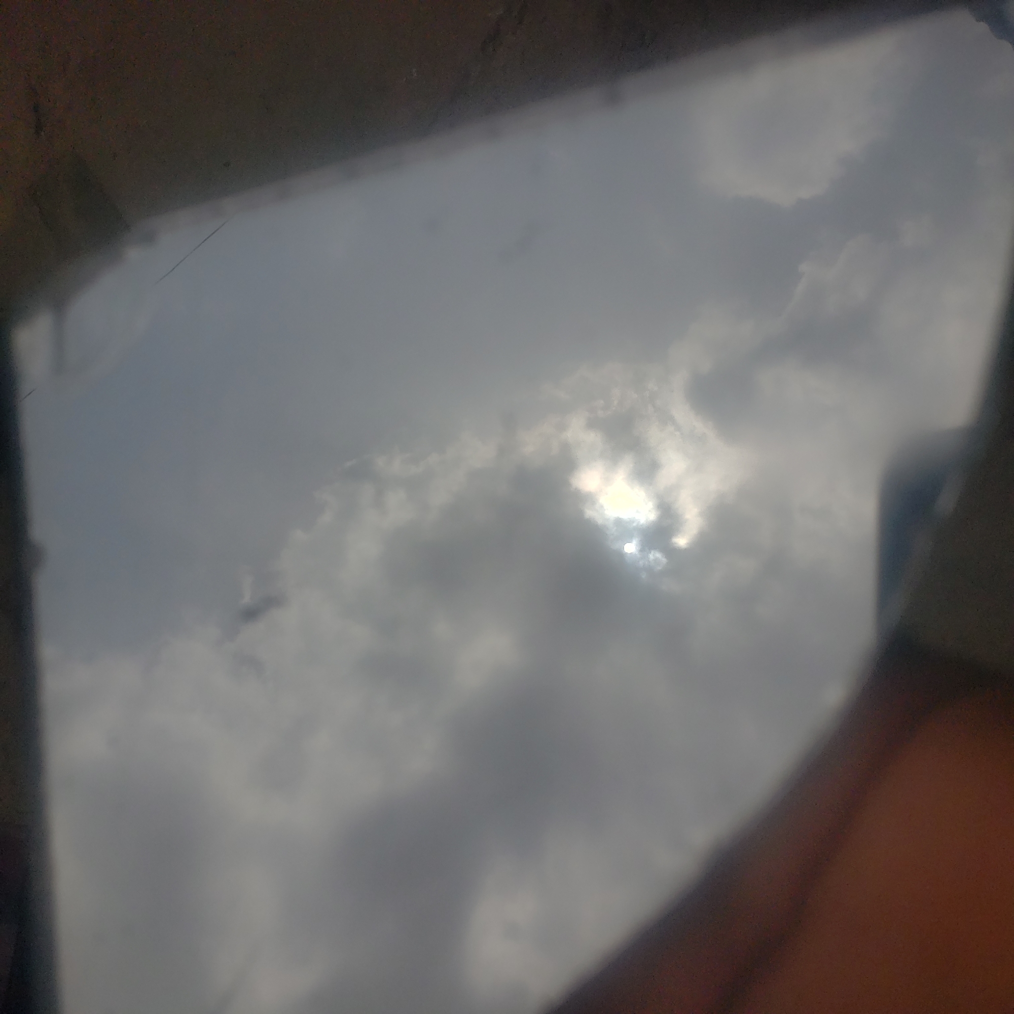 The image shows a cloudy sky, possibly with the sun partially obscured by clouds. The view is framed by what appears to be a partial structure or frame, possibly a window. The location is Narayi, Nigeria, but no other specific details about the location are discernible. No people, objects, actions, or interactions besides the sky and the framing structure are present in the image.