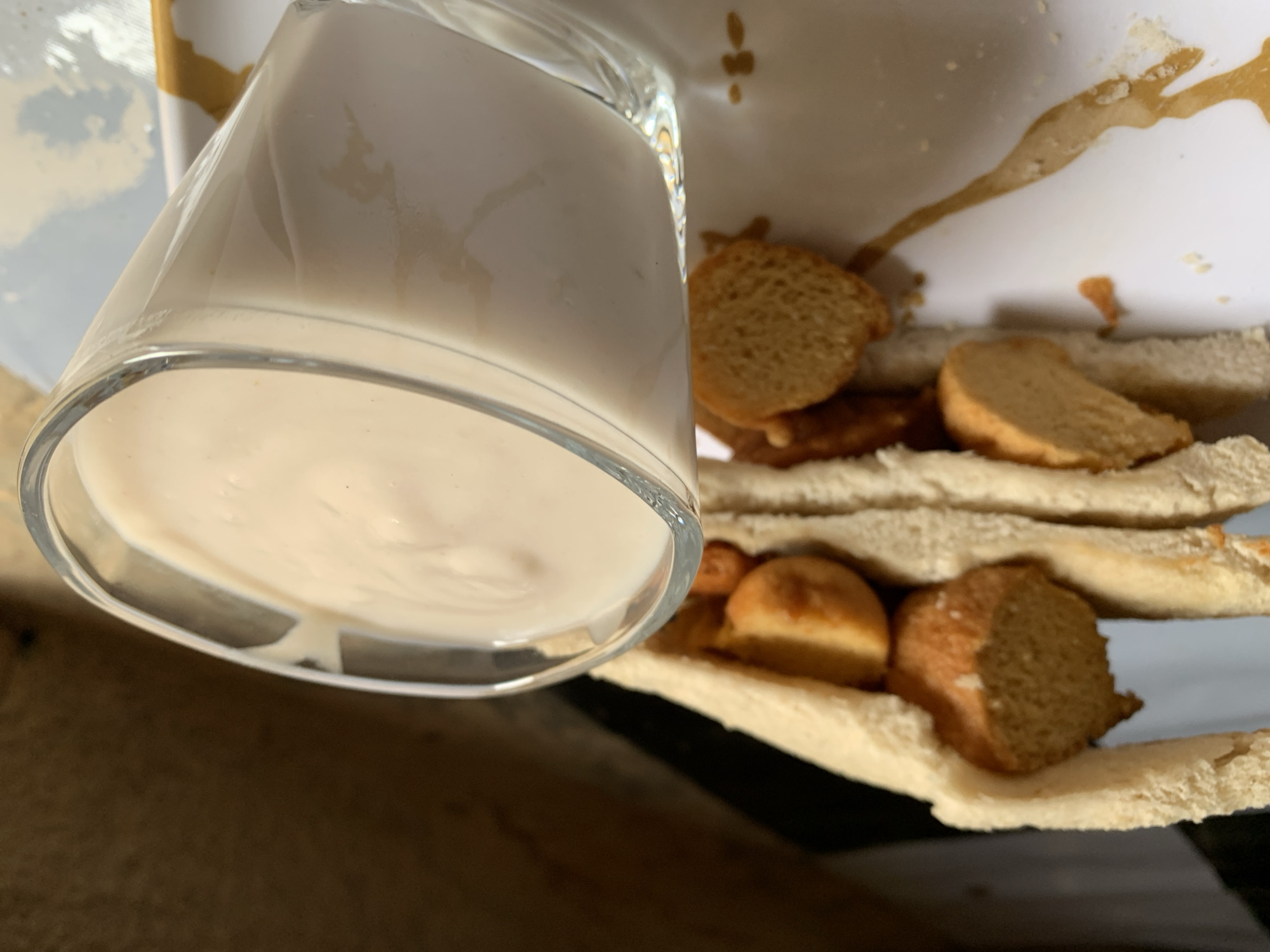 A glass filled with a white liquid sits upside down on a white plate next to a sandwich containing fried yam pieces. The plate has a gold design element. The scene is indoors. There is no information to ascertain this image location in Rafin Par, Nigeria. No people are visible.