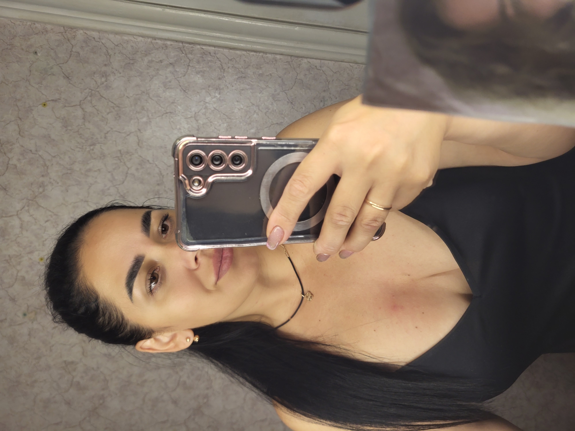 A woman is taking a selfie in a bathroom in Horishni Plavni, Ukraine. She is wearing a black dress and jewelry. The background appears to be a tiled wall.
