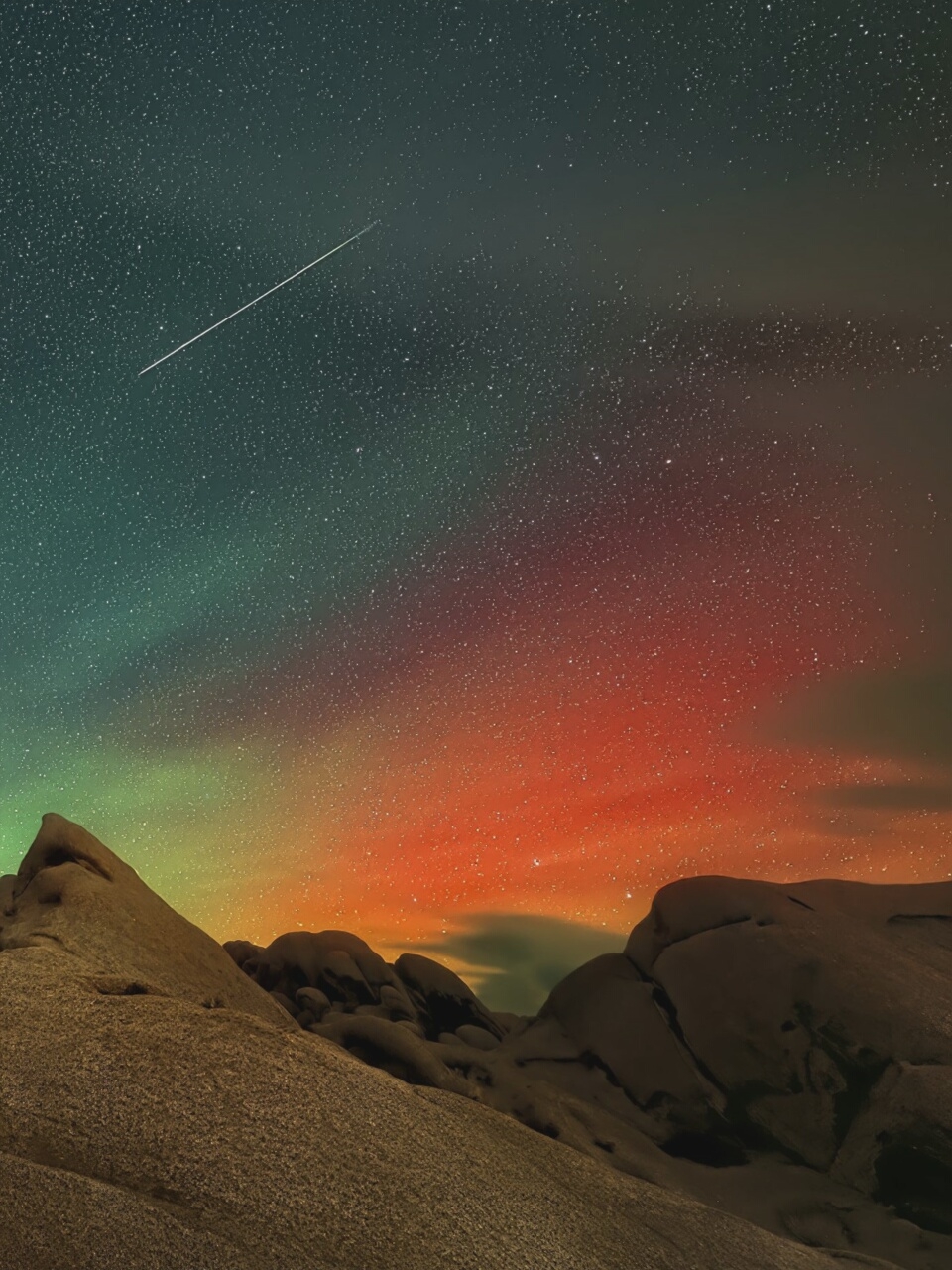 An artistic interpretation of a night sky over a rocky landscape. A streak of light, likely a meteor or satellite, traverses the upper left quadrant of the image. The sky displays a gradient of colors, transitioning from a deep teal in the upper left to vibrant orange and red hues towards the right, with numerous stars scattered across the scene. The foreground is dominated by rugged, textured rock formations, illuminated from above. The image does not depict a specific location within French Pass / Anaru, New Zealand, as it appears to be a composite or digitally altered image rather than a photograph of a real-world scene. There are no people, animals, or distinct man-made objects present.