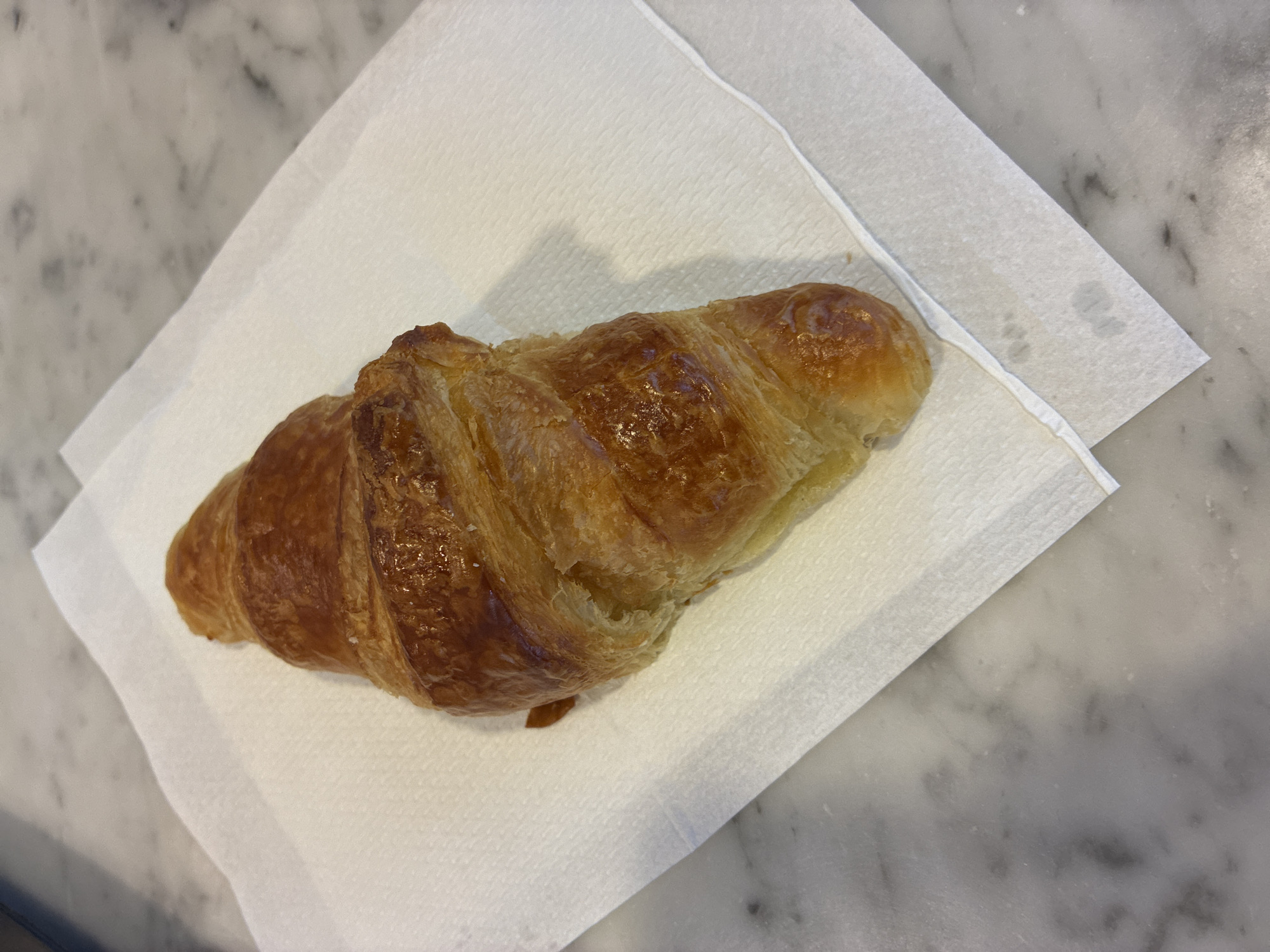 A croissant rests on a folded white napkin on a marble surface. No people are visible. The specific location within Sant Josep de sa Talaia, Spain, cannot be determined from the image alone.