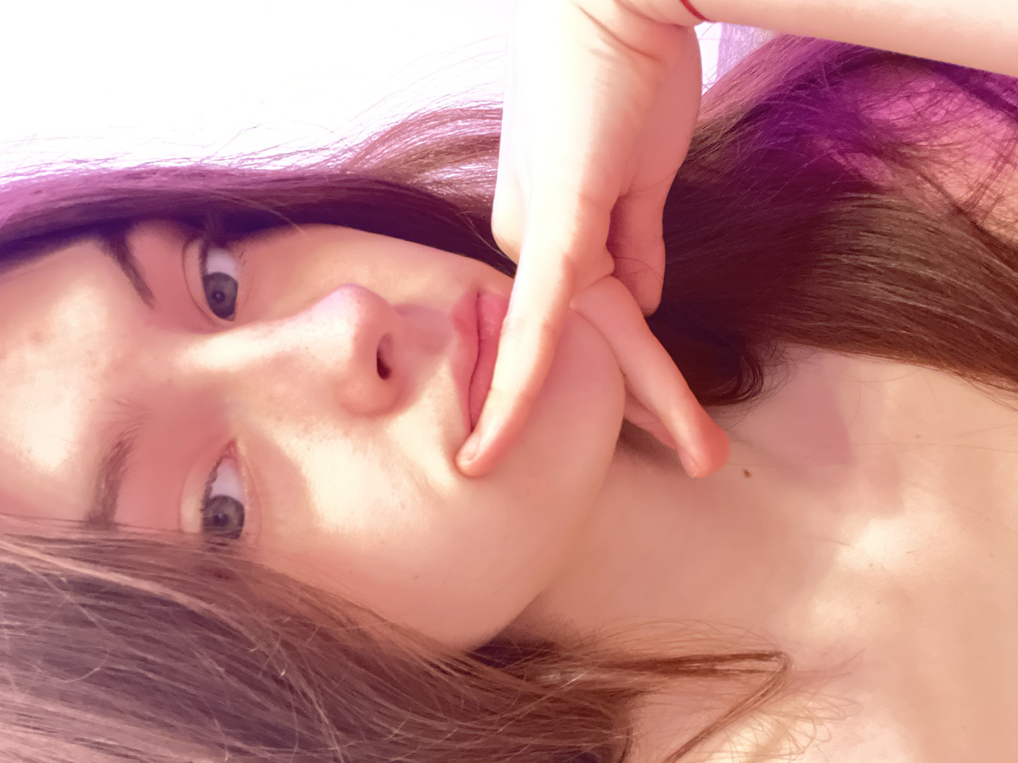 A close-up, tilted portrait depicts a young woman with brown hair and light skin. Her face is the primary focus, and her hand is positioned near her cheek in a gesture. The background has a mix of white and pinkish light, suggesting indoor lighting. No specific details indicate the city of Saint Petersburg, Russia. The image primarily showcases the woman and her pose.