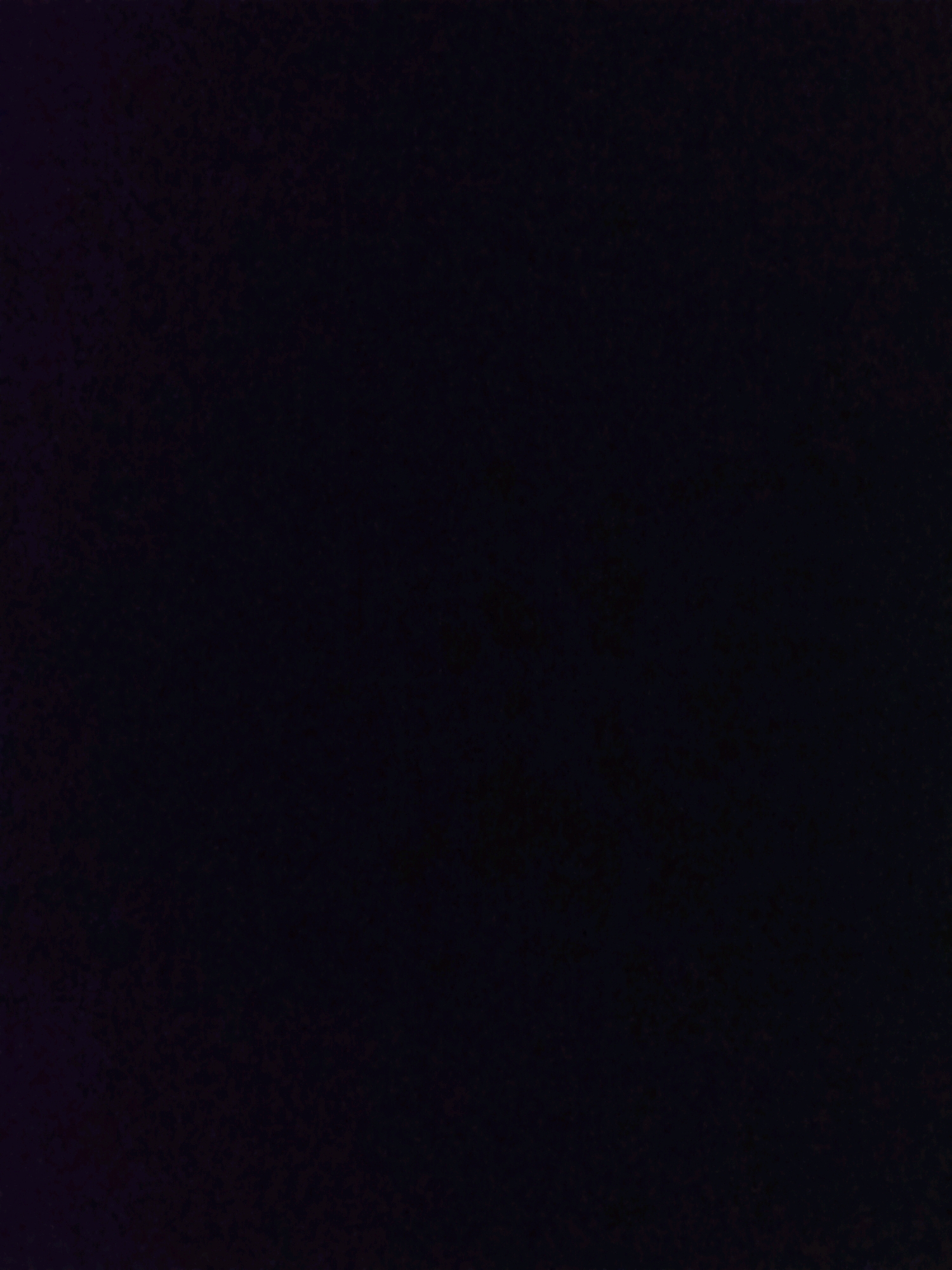 The image is a very dark, almost black, abstract photograph. There are no discernible subjects, objects, people, or actions. The environment is not visible. The texture appears slightly grainy or mottled, but this is difficult to determine with certainty due to the darkness. There is a very subtle hint of purple or deep blue in the upper left corner, suggesting a very dim light source or a dark colored object. It is not possible to determine the location in the city of Tamchy, Kyrgyzstan, or any other specific details from this image.