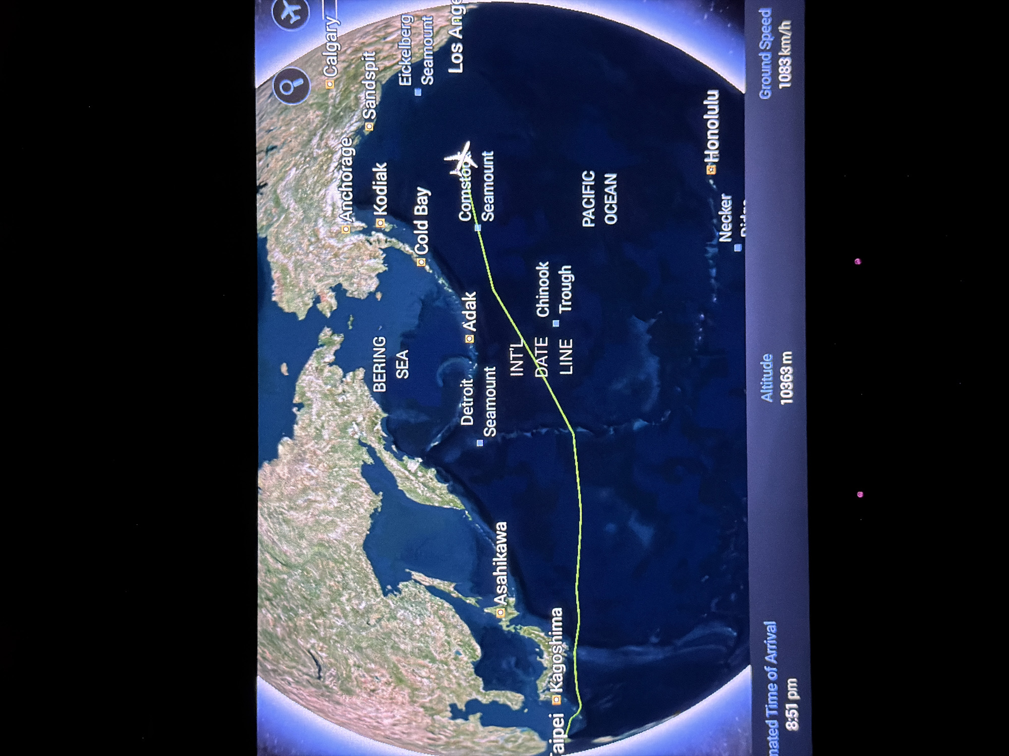 Here is a description of the image:
The image displays a flight tracking map. The flight path, indicated by a green line, originates near Taipei and Kagoshima, passes over Asahikawa, and is currently positioned over the Pacific Ocean, near Comstoc Seamount. Several cities are marked on the map including, Anchorage, Kodiak, Cold Bay, Adak, Detroit Seamount, Honolulu, Necker, Calgary, Sandspit, Eickelberg Seamount, and Los Angeles. Los Angeles appears to be in the United States of America. The flight's altitude is 10363 meters, and its ground speed is 1083 km/h. The estimated time of arrival is 8:51 pm. The map also shows the Bering Sea and the International Date Line.