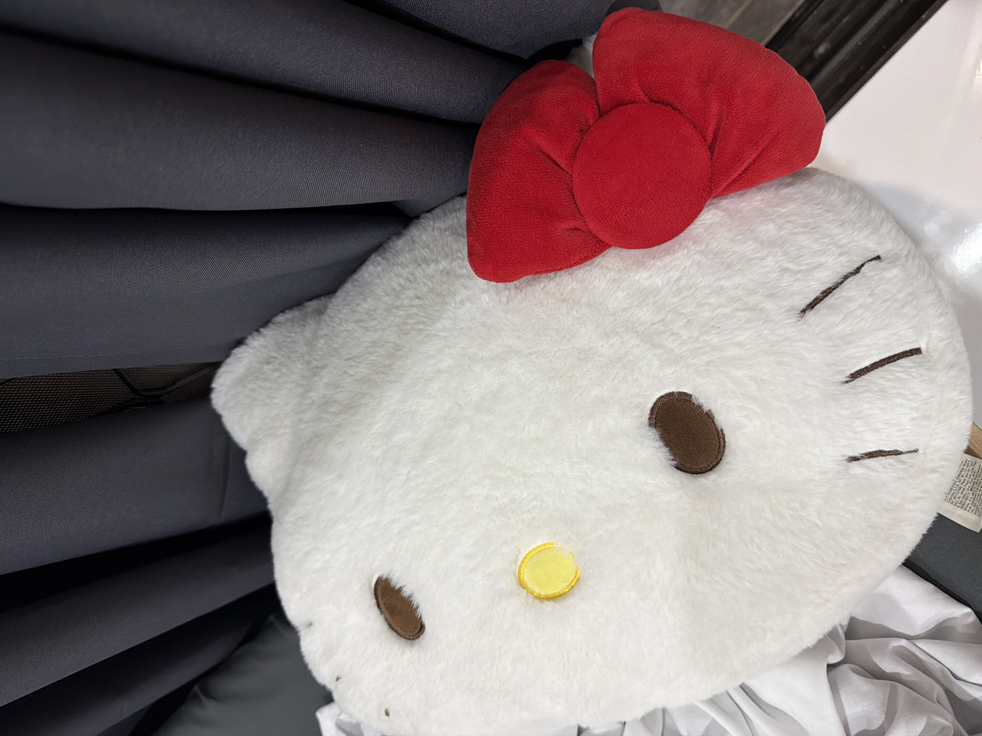 A white, plush Hello Kitty pillow with a red bow is partially visible next to a stack of folded gray fabrics. The pillow features embroidered details including brown eyes, whiskers, and a yellow nose. The context suggests the image was likely taken indoors, potentially in a retail environment or domestic setting. The location in Davao City, Philippines is not discernible from the image.