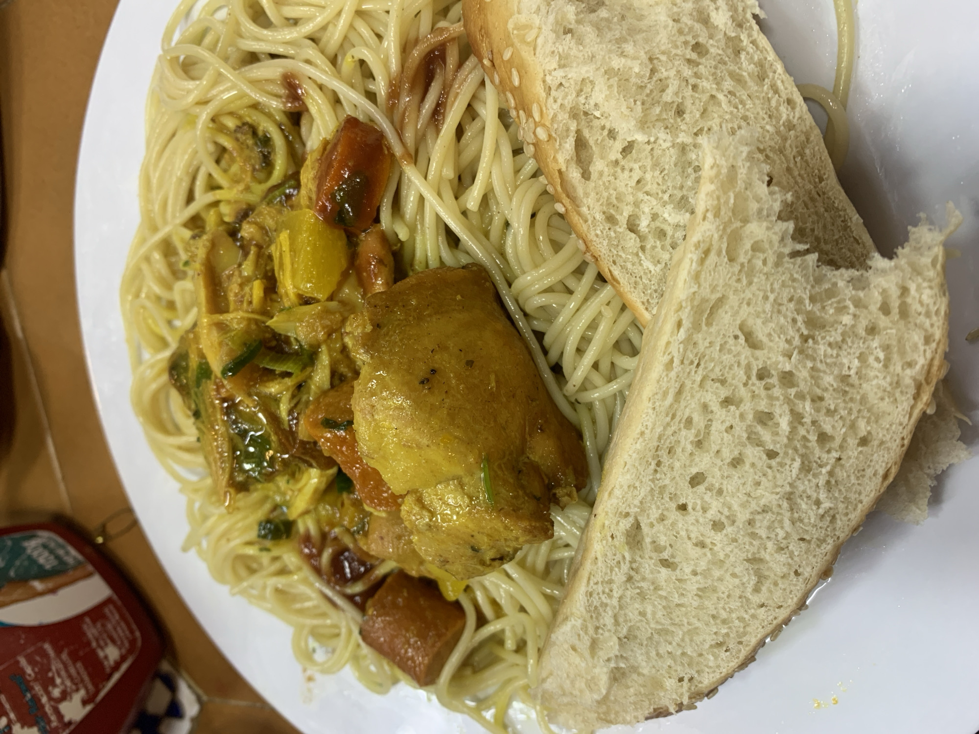 A plate of food is presented. The plate contains spaghetti with what appears to be chicken curry. Two slices of sesame bread are placed next to the spaghetti. The location in the city of Porlamar, Venezuela, cannot be determined from the image.