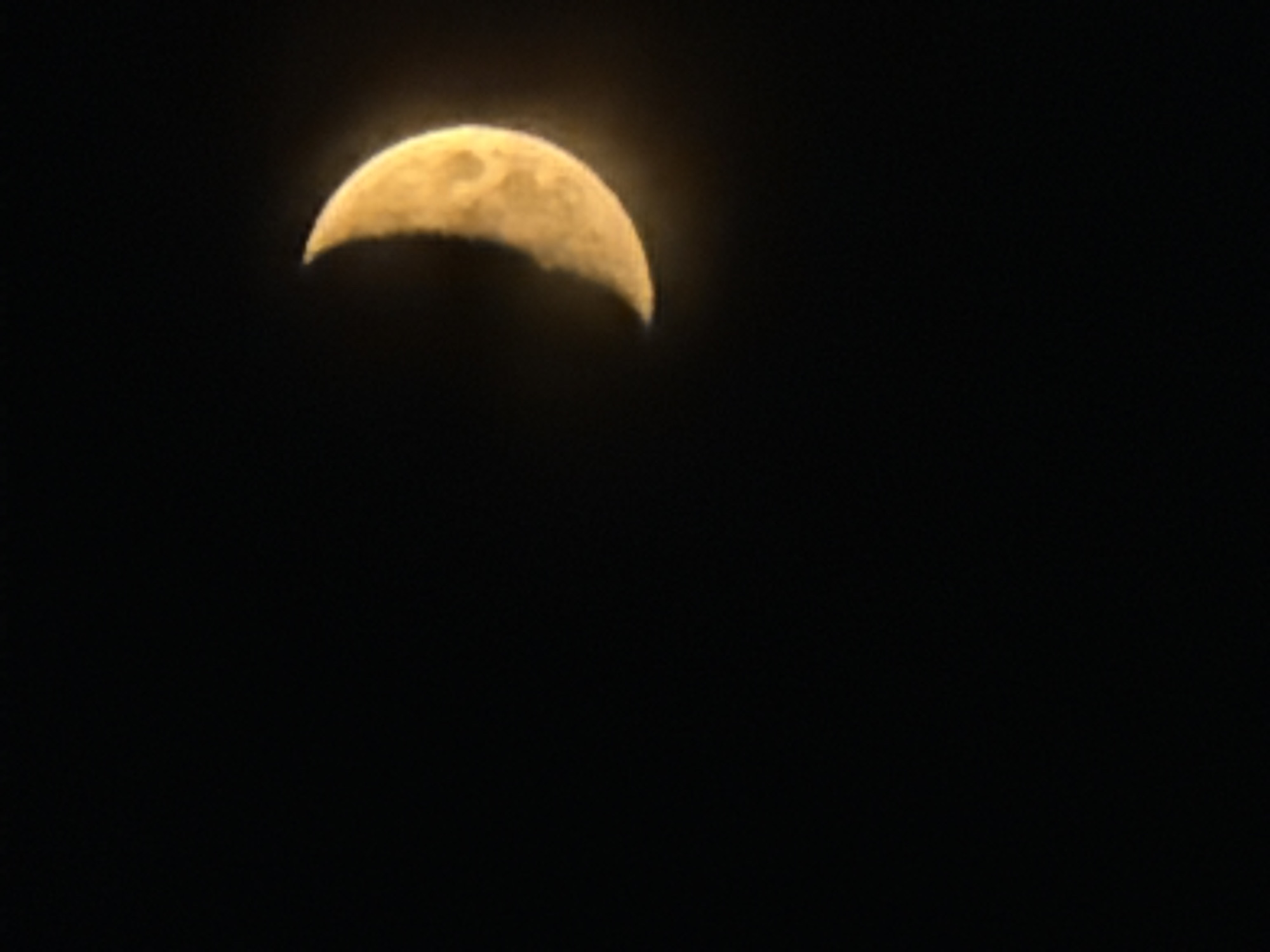 The image shows a crescent moon against a black sky. The moon is illuminated from the left and appears to be a yellowish-orange color. There are some visible craters or surface features on the illuminated portion of the moon. The image does not contain any elements that would suggest a specific location in the city of Astana, Kazakhstan, or any other geographical context.
