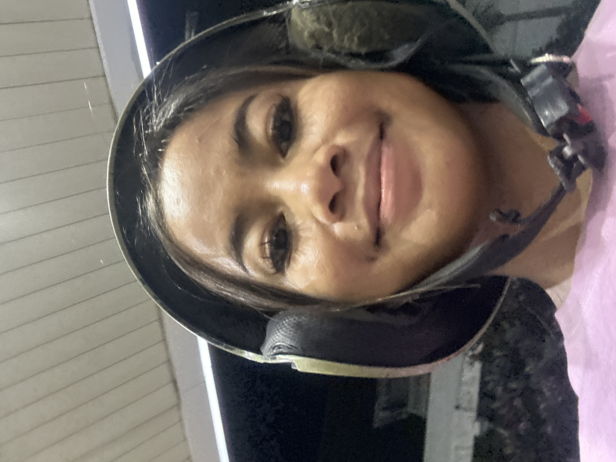 A young woman is wearing a helmet with ear coverings and a chin strap. She is likely standing outside, as there are exterior walls in the background. The location appears to be Central Jakarta, Indonesia.