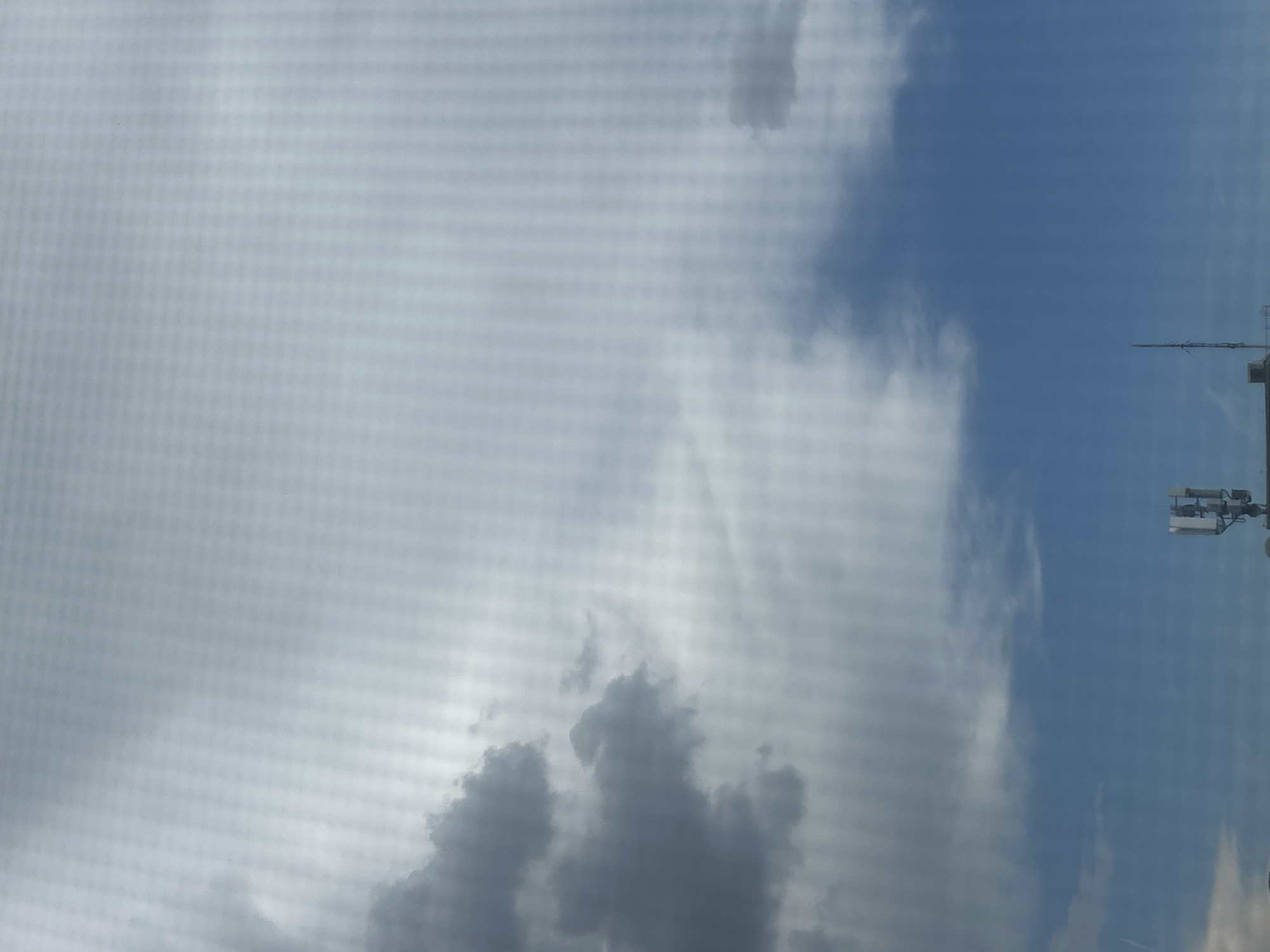 The media file shows a partially cloudy sky with a blue sky visible on the right side. In the upper right portion of the image, a tall structure, likely a tower or building, is visible with antennas or broadcasting equipment attached. The overall scene suggests an outdoor setting, possibly urban, given the presence of the structure. The lighting indicates it is daytime, but the presence of clouds makes it difficult to determine the exact time. The weather appears to be mixed, with both clear blue sky and overcast or cloudy conditions present. There are no visible people or specific activities depicted in the media file. There is no visible text in the image. The location context is Linz, Austria.