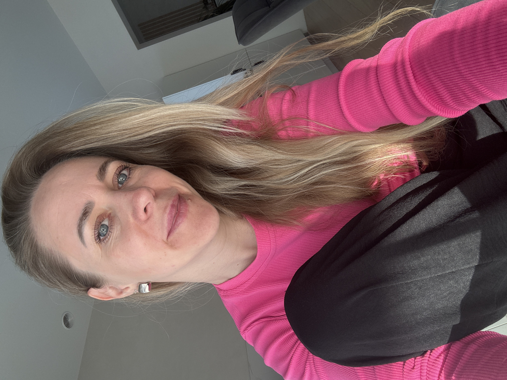 A woman with blonde hair and blue eyes is facing the camera, wearing a pink long-sleeved shirt and black pants. She appears to be indoors. The location cannot be verified as Chaikovsky, Russia, based on the provided image.