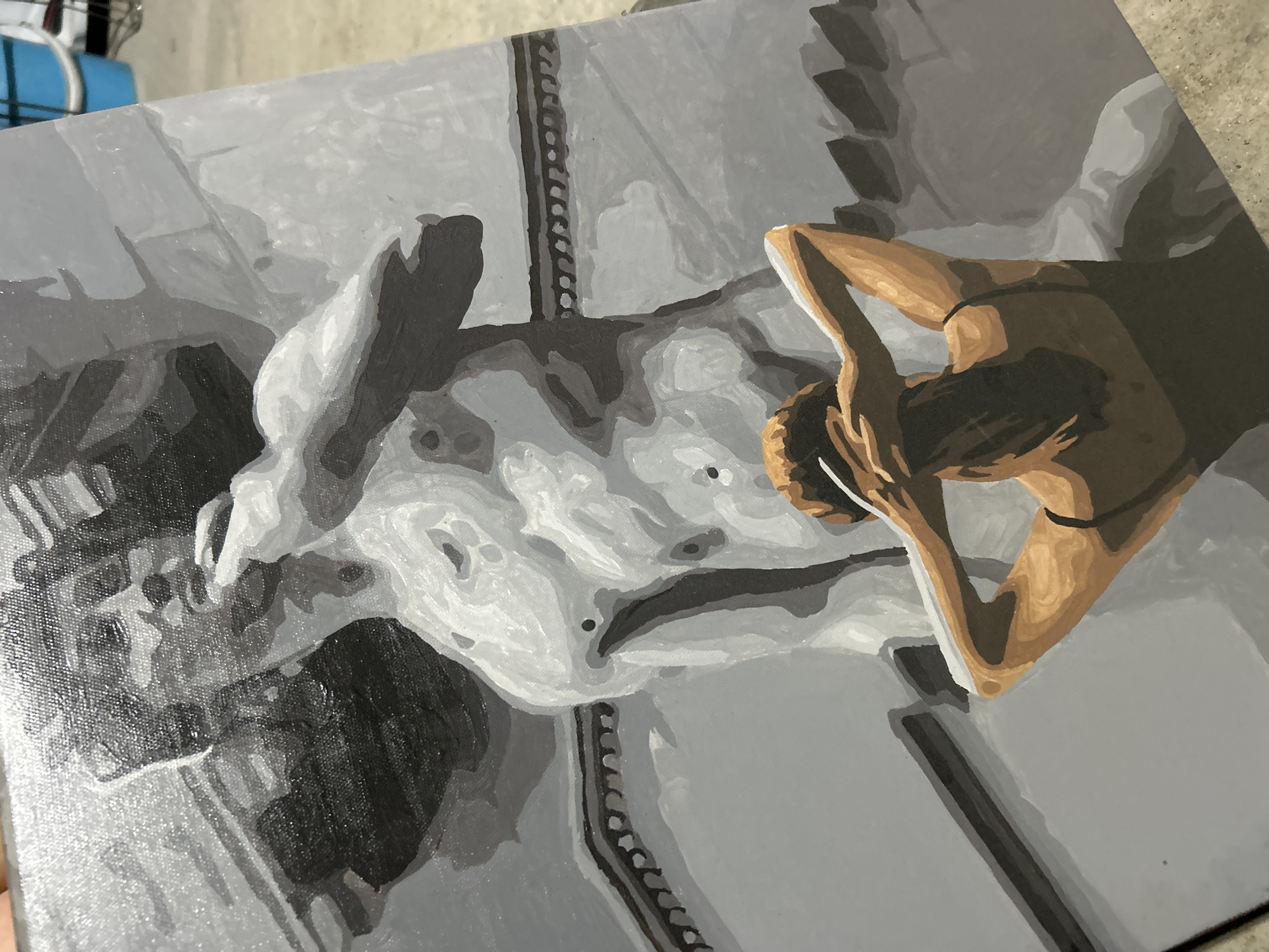 The image depicts a grayscale painting on a canvas. The subject is a person in a reclining pose. The person's skin is depicted in shades of brown, with the rest of the scene rendered in varying shades of gray. The person's arms are raised behind their head. The setting appears to be a bed or similar reclining surface. The style of the painting is somewhat abstract, with bold brushstrokes and a limited color palette. There is no information on the location of the city of Noviy, Russia.
