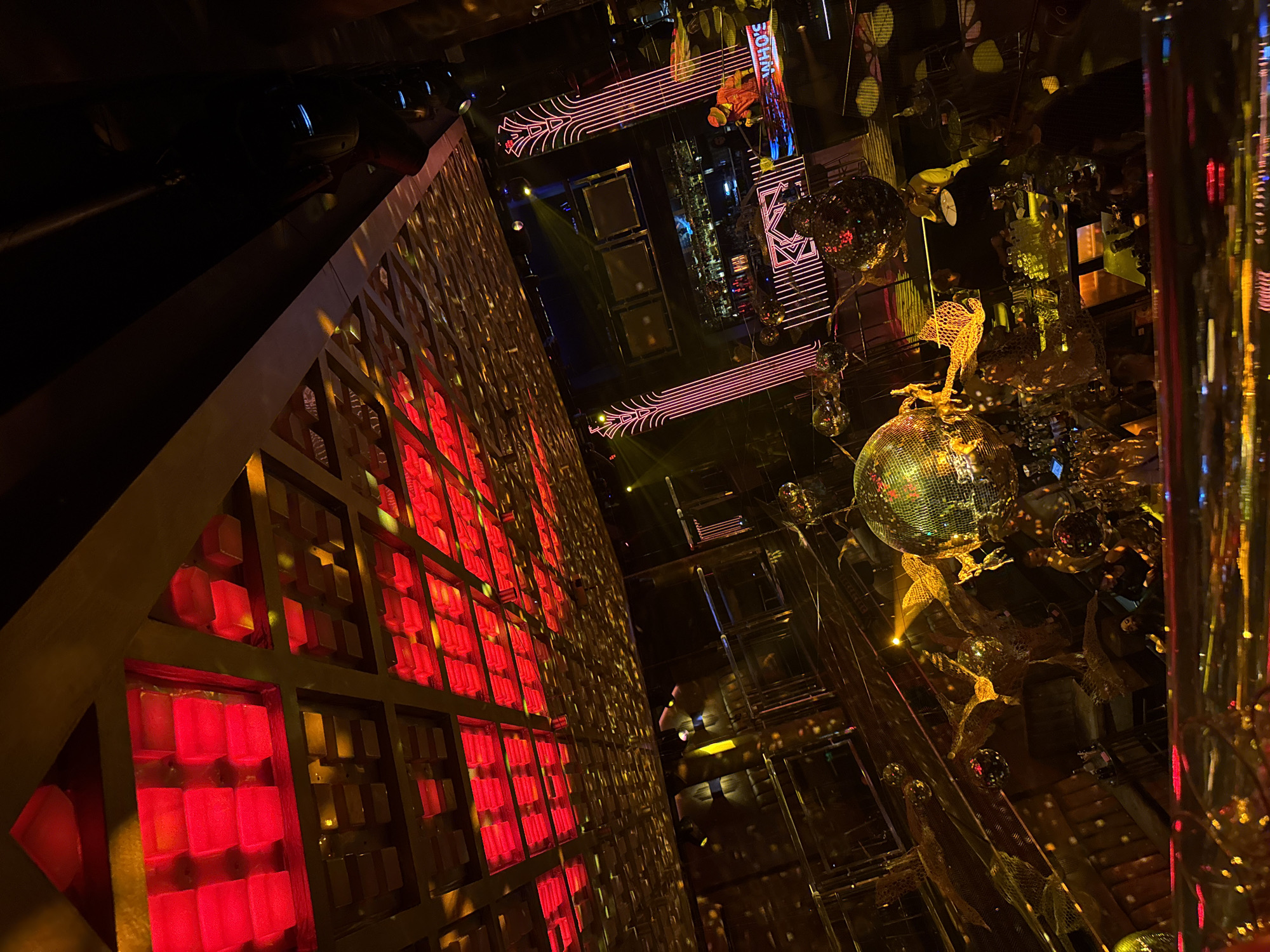 The image shows the interior of a club in Sofia, Bulgaria. The club is decorated with disco balls, neon lights, and a wall with illuminated red cubes. The overall atmosphere is dark and festive, indicative of a nightclub or bar setting. The "SOHO" branding is visible.