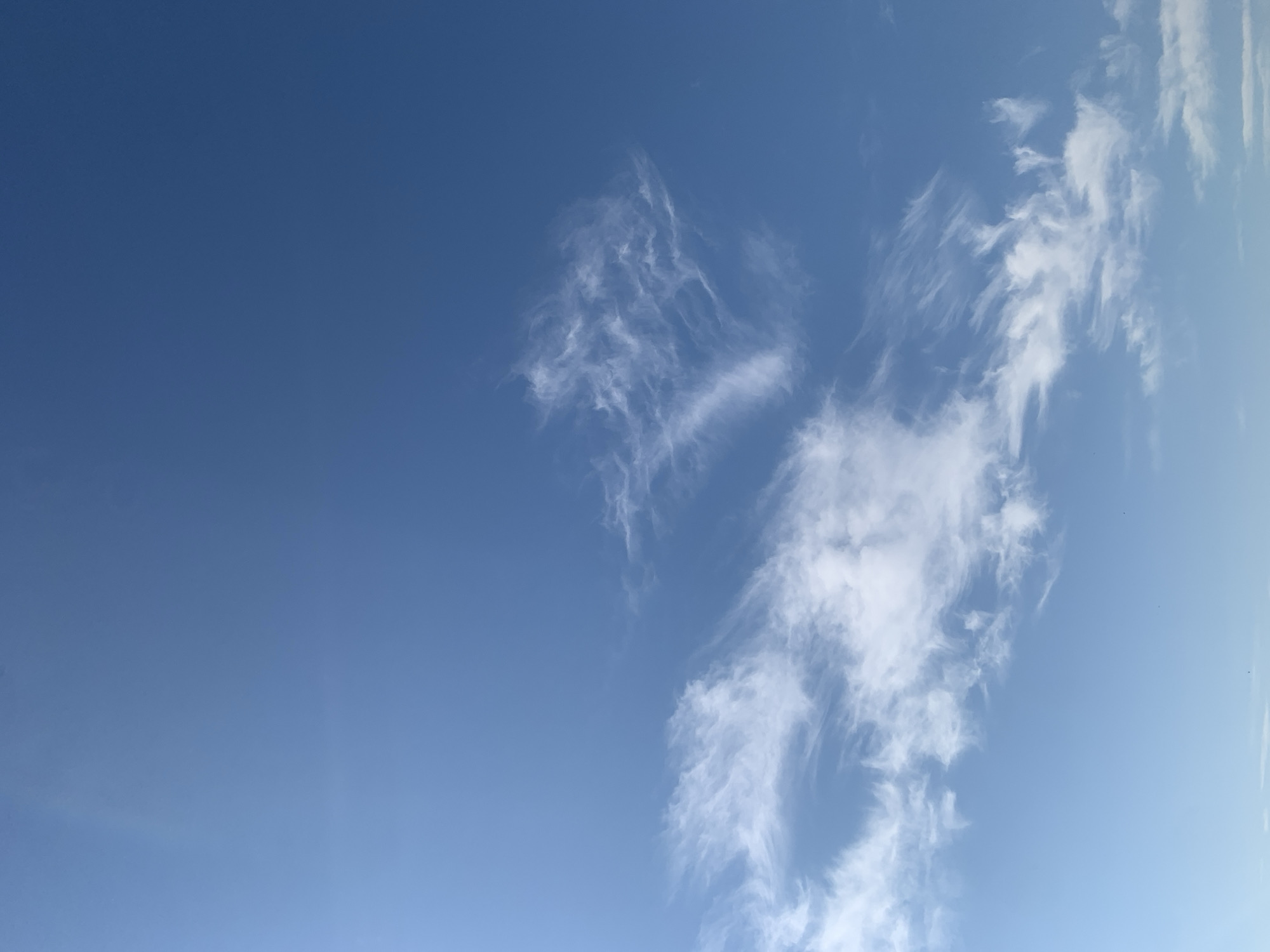 The image is a photograph of a clear blue sky with wispy white clouds. There are no people, objects, or discernible buildings visible in the frame, making it impossible to determine the location within the city of Kolomyia, Ukraine, or any specific actions or interactions. The environment depicted is solely the sky.