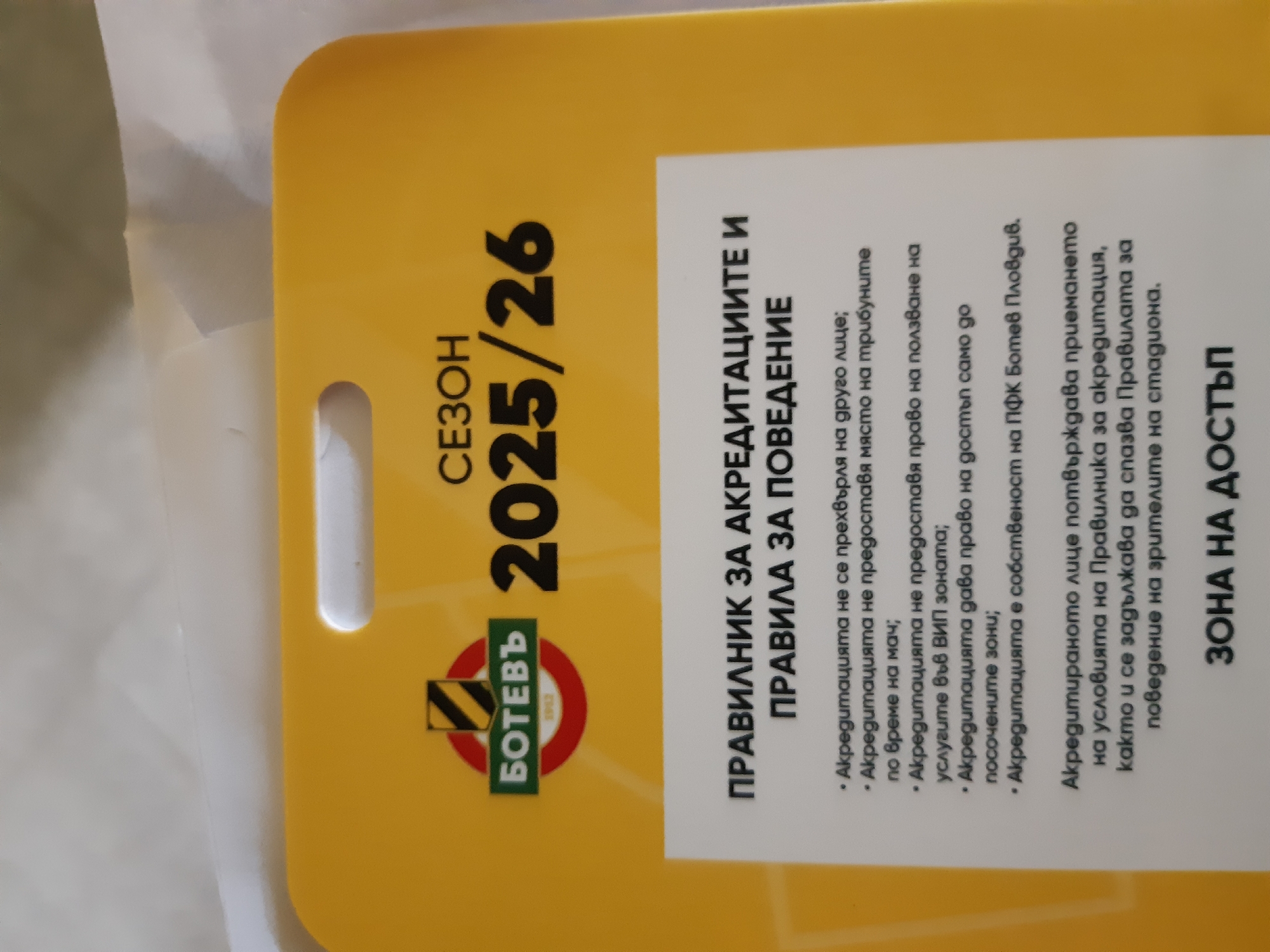 Here is a description of the image:
The image shows a yellow accreditation pass for the "Botev" football club for the 2025/26 season. The pass includes the club's logo, the season dates, and the text "ПРАВИЛНИК ЗА АКРЕДИТАЦИИТЕ И ПРАВИЛА ЗА ПОВЕДЕНИЕ" (Rules for Accreditation and Rules of Conduct). It lists rules regarding the use of the accreditation, stating that it is not transferable, does not guarantee a seat, only allows access to designated areas, and remains the property of PFC Botev Plovdiv. It also states that the accredited person acknowledges and agrees to follow the rules of conduct for stadium spectators. It designates "ЗОНА НА ДОСТЪП" (access area). Botev Plovdiv is a football club based in Plovdiv, Bulgaria.