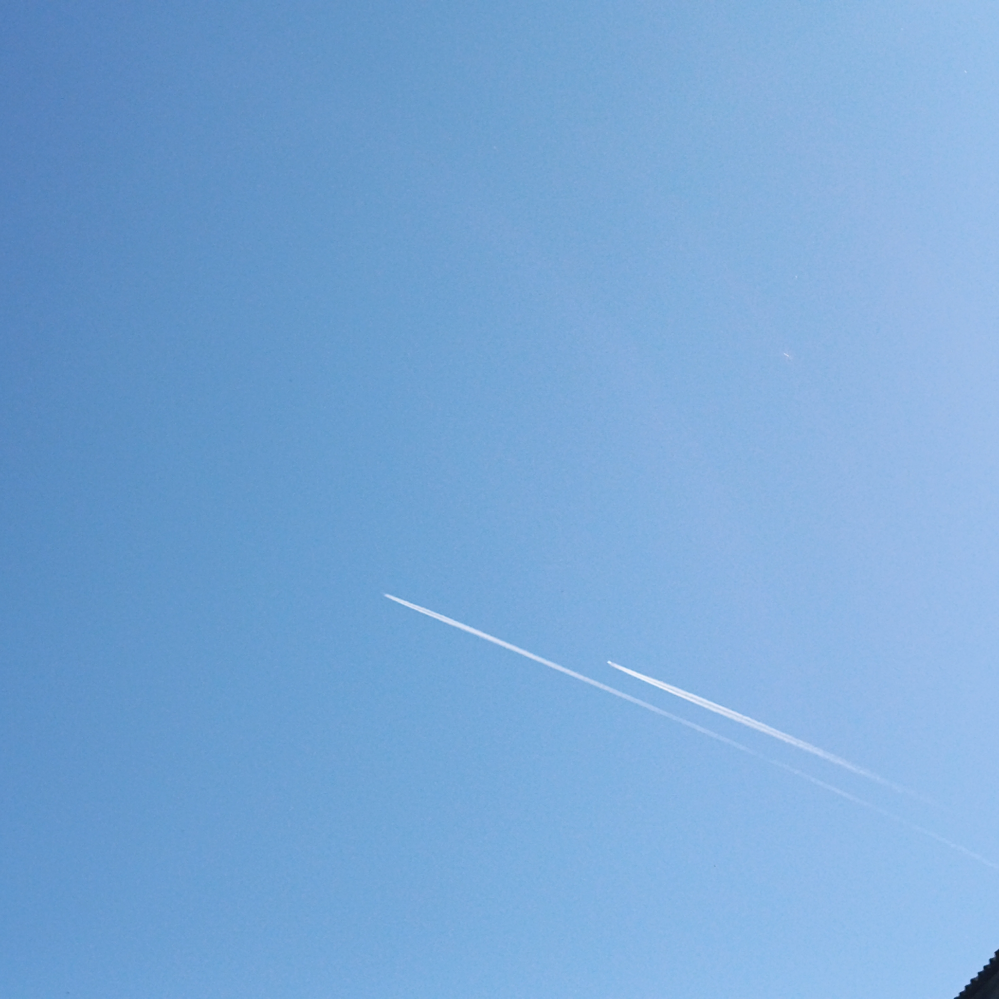 The image shows a clear blue sky with two contrails from airplanes. The location cannot be determined from the image alone. There are no people visible.