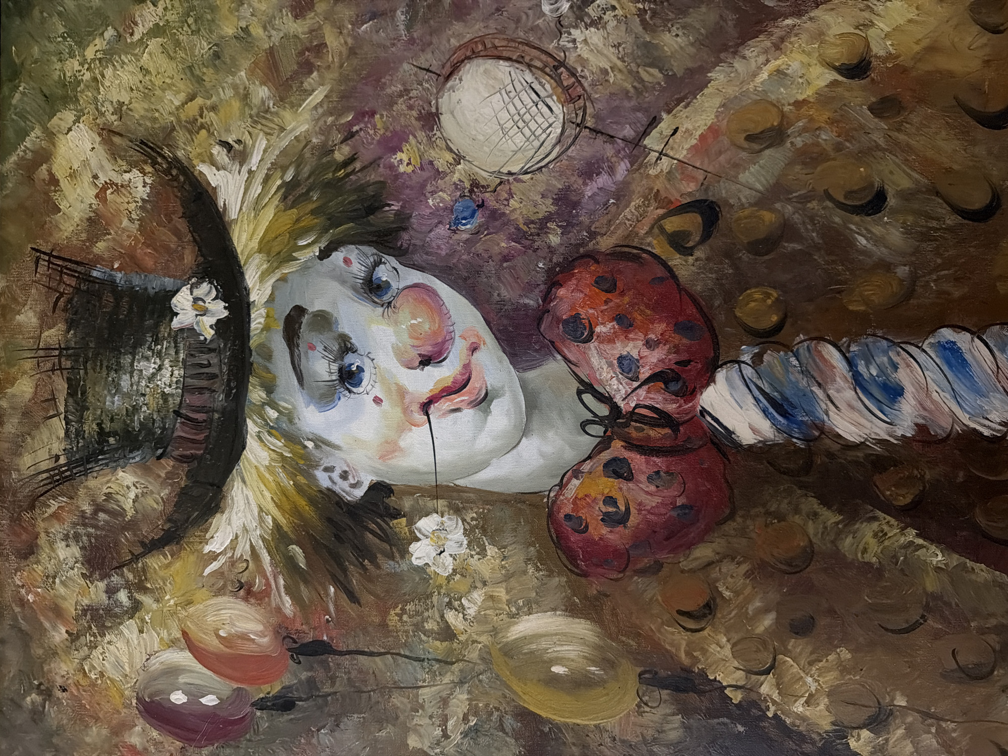 The image is a painting of a clown's face lying on its side. The clown has pale skin, rosy cheeks, and large blue eyes with prominent eyelashes. The face is adorned with a small black top hat with a white flower, a large red polka-dotted bow tie, and a ruffled collar. A small white flower is painted beneath the face. Several colorful balloons are positioned near the bottom of the painting. The background is a mix of brown, beige, and purple hues, creating an abstract and somewhat melancholic atmosphere. The painting is not clearly indicative of any specific location in Levkovo, Russia. The style suggests oil on canvas.