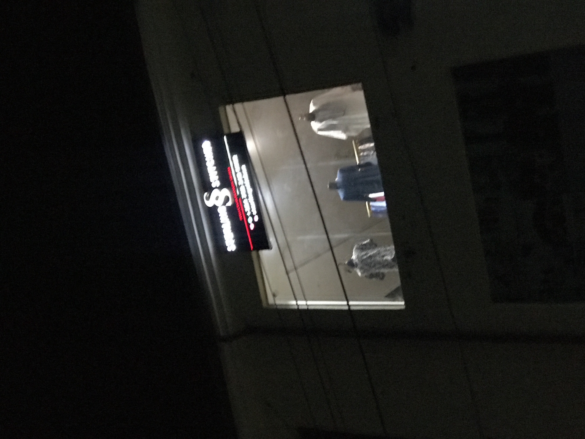 A low-angle nighttime view shows a shopfront in Gwarinpa, Nigeria. The sign for "SS STITCHES TAILORING" is illuminated. Through the window, several garments are visible on display racks. Power lines cut across the view. The surrounding environment appears dark and urban.