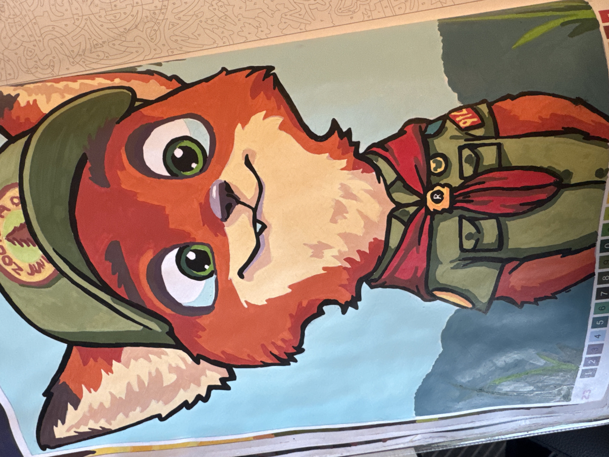 A medium shot portrait shows a cartoon fox wearing a scout uniform and hat. The fox has orange fur, large green eyes, and a friendly smile. It is wearing a green hat with a circular emblem, a green shirt with patches on the sleeves, and a red scarf. The background is a light blue sky with dark green hills. The image appears to be part of a coloring book, as evidenced by the numbered squares at the bottom and the text on the right side of the image. The subject is centered in the frame.