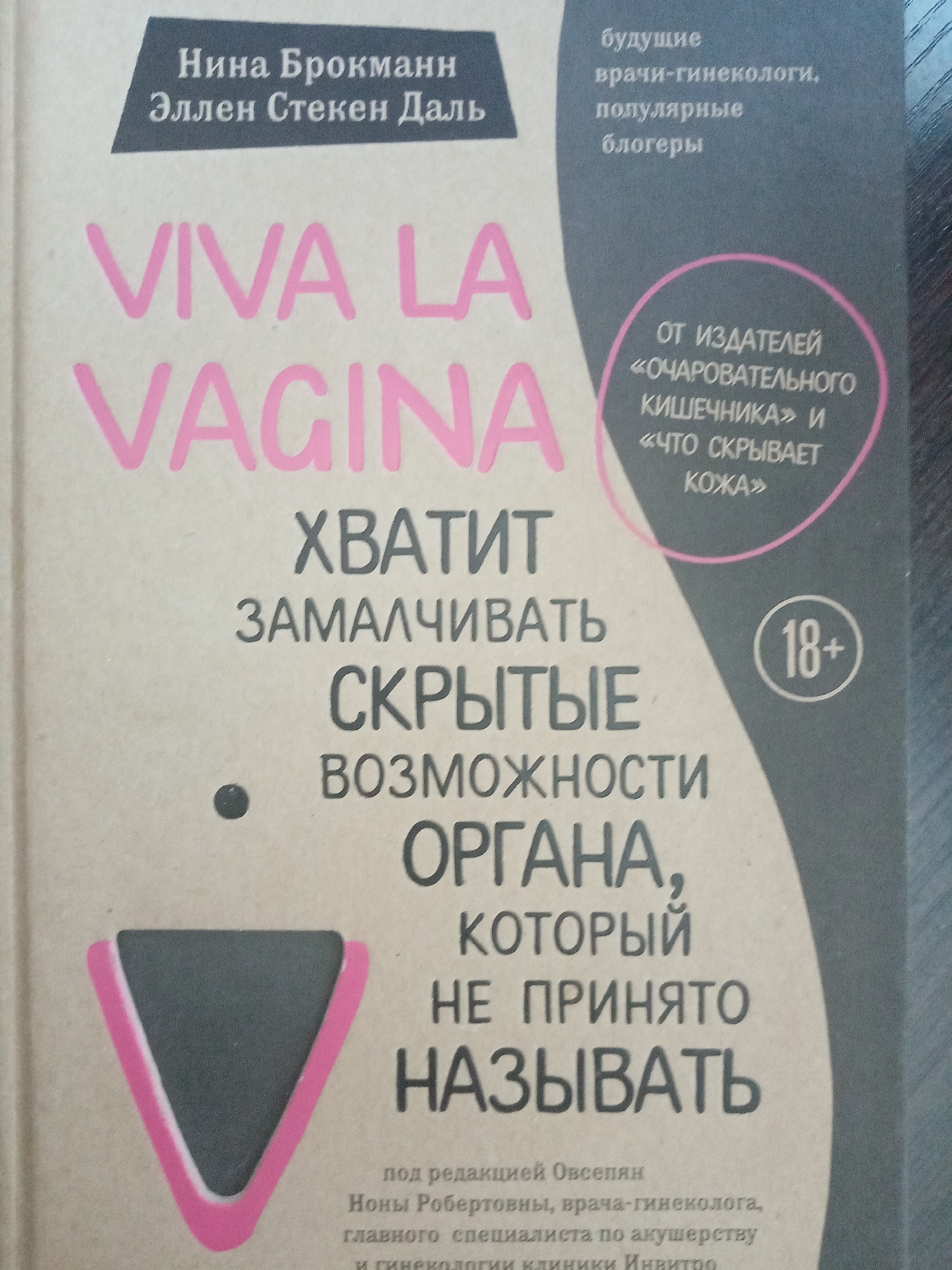 The image shows the cover of a book titled "VIVA LA VAGINA" with the authors listed as Нина Брокманн (Nina Brokmann) and Эллен Стекен Даль (Ellen Steken Dahl). Below the title, in Russian, it says "ХВАТИТ ЗАМАЛЧИВАТЬ СКРЫТЫЕ ВОЗМОЖНОСТИ ОРГАНА, КОТОРЫЙ НЕ ПРИНЯТО НАЗЫВАТЬ" which translates to "STOP BEING SILENT ABOUT THE HIDDEN POSSIBILITIES OF THE ORGAN THAT IS NOT USUALLY NAMED." There is a pink outline of a triangle with a dark triangle inside it. A gray-colored shape on the right contains the text "будущие врачи-гинекологи, популярные блогеры" ("future gynecologists, popular bloggers") and a circle with the text "ОТ ИЗДАТЕЛЕЙ «ОЧАРОВАТЕЛЬНОГО КИШЕЧНИКА» и «ЧТО СКРЫВАЕТ КОЖА»" ("FROM THE PUBLISHERS OF 'CHARMING GUT' AND 'WHAT THE SKIN HIDES'") along with a circle containing "18+". The text at the bottom indicates it is under the editorship of Овсепян Ноны Робертовны (Ovsepyan Nona Robertovna), a gynecologist and chief specialist in obstetrics and gynecology at the Invitro clinic. The image does not provide any information about the location being Elektrostal, Russia.