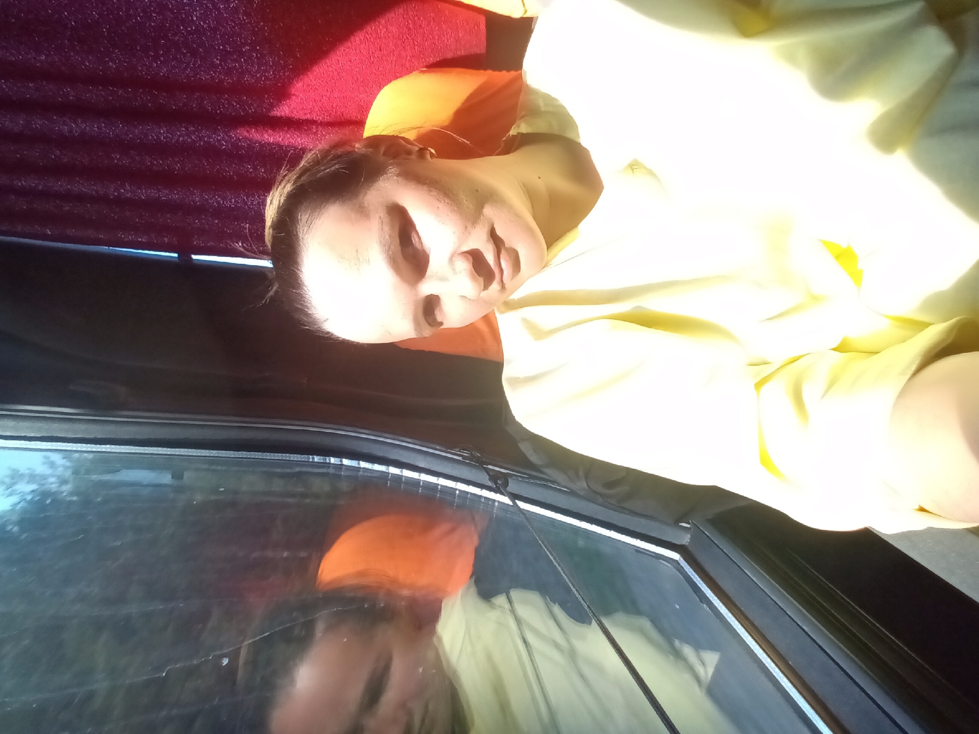 A woman is reclining in what appears to be a vehicle, possibly a van or RV, with a window above her. She is wearing a light yellow shirt, and there are red and orange cushions or seats behind her. Her reflection is visible in the window. Based on the geotag, the location is Sivinskoe, Russia.