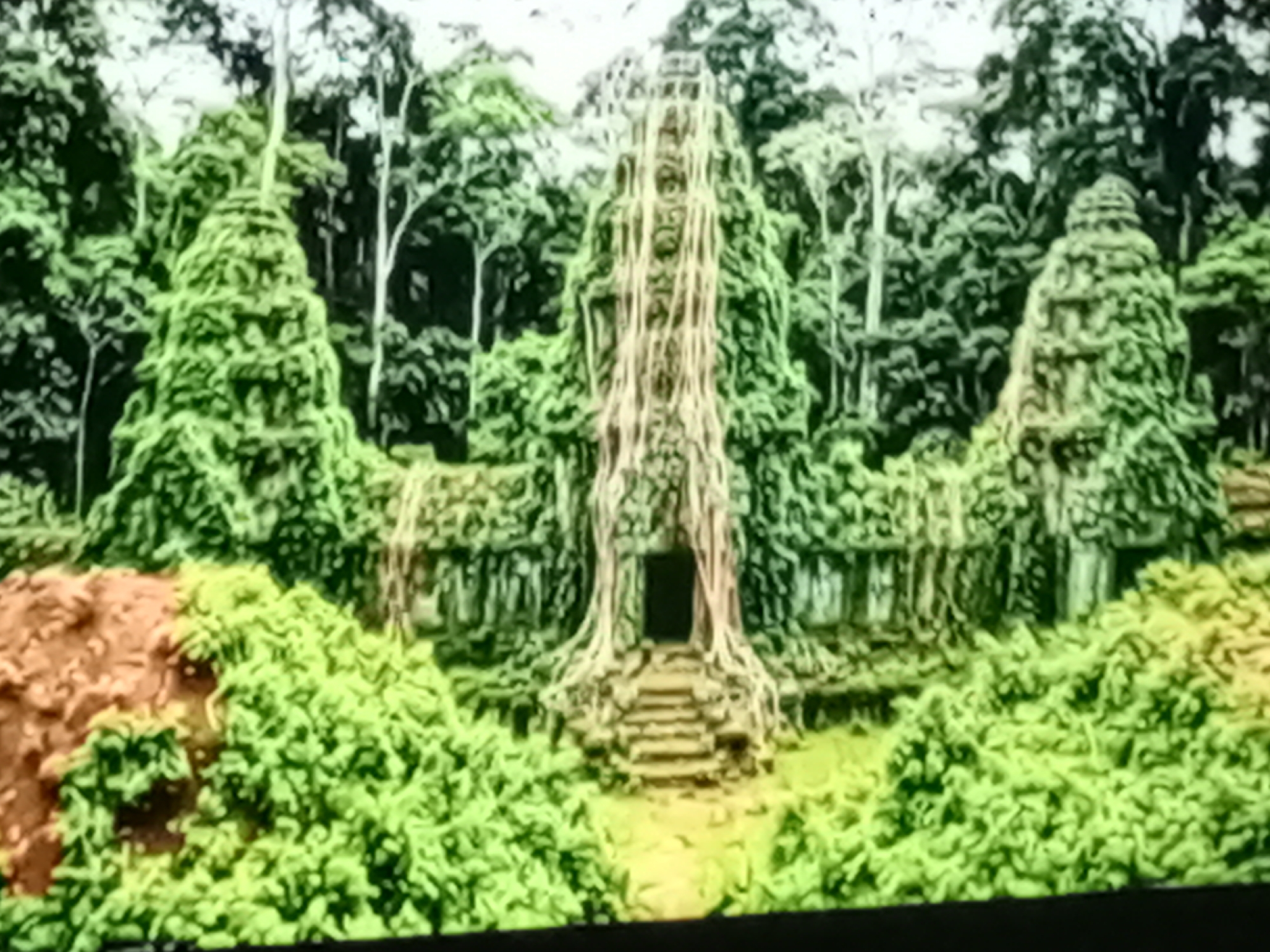 The image depicts an ancient temple partially reclaimed by lush vegetation and tree roots, located in a dense jungle environment. The temple features intricate stonework and a central structure with steps leading to a dark entrance. The surrounding area is filled with vibrant green foliage, with tall trees forming a canopy overhead. The overall scene evokes a sense of mystery and abandonment, with nature slowly consuming the man-made structure. There are no people or discernible activities shown in the image. The location is specified as Unknown, Unknown, within the city of Unknown.