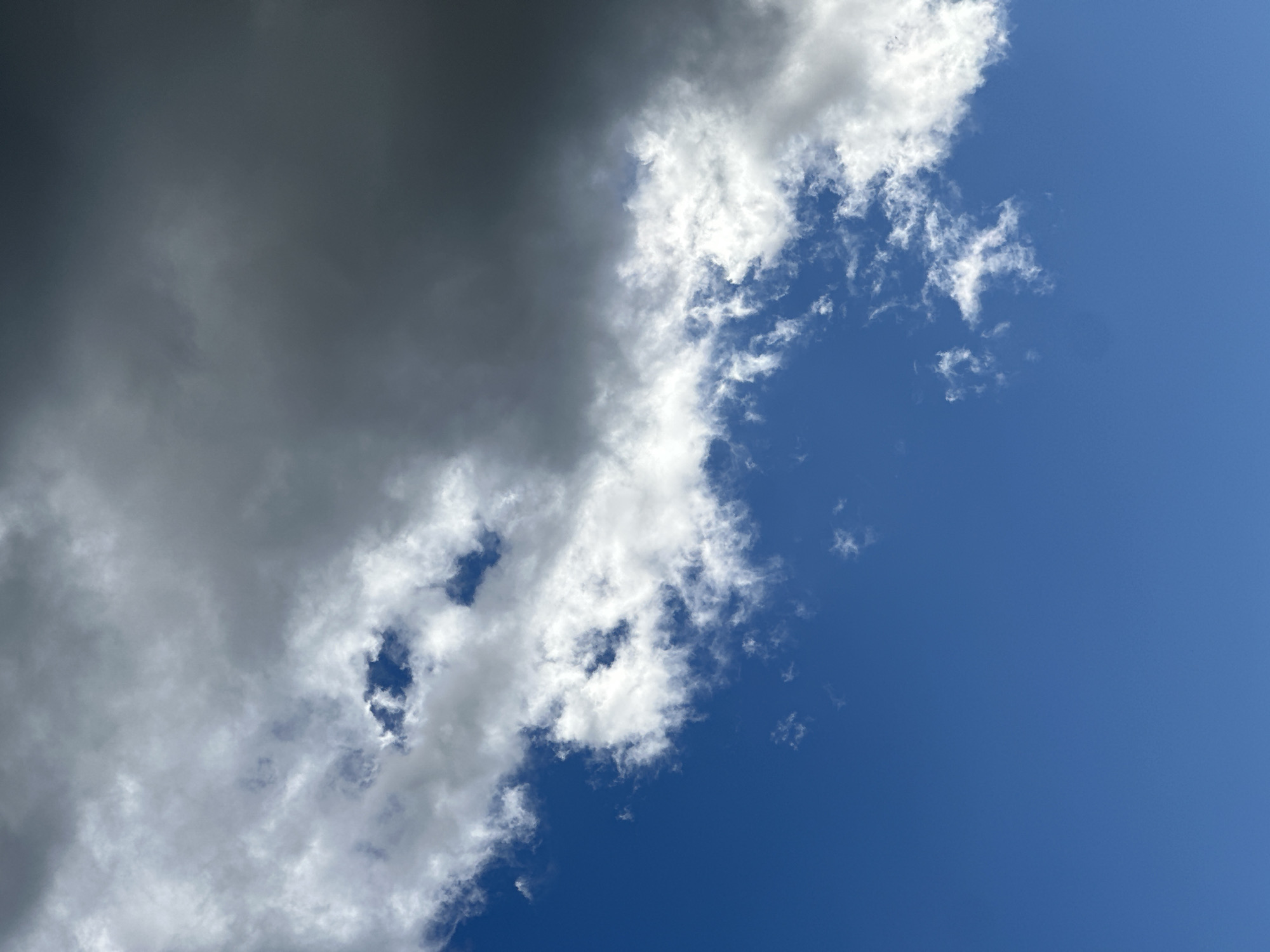 The image shows a view of the sky with a mix of dark storm clouds and clear blue sky. The clouds are predominantly on the left side, ranging from dark gray to light gray and white, suggesting varying thicknesses and densities. On the right, the sky is a clear, deep blue. The cloud formation suggests an approaching or receding storm. There is no information to indicate that it is in the city of Nizhny Novgorod, Russia.