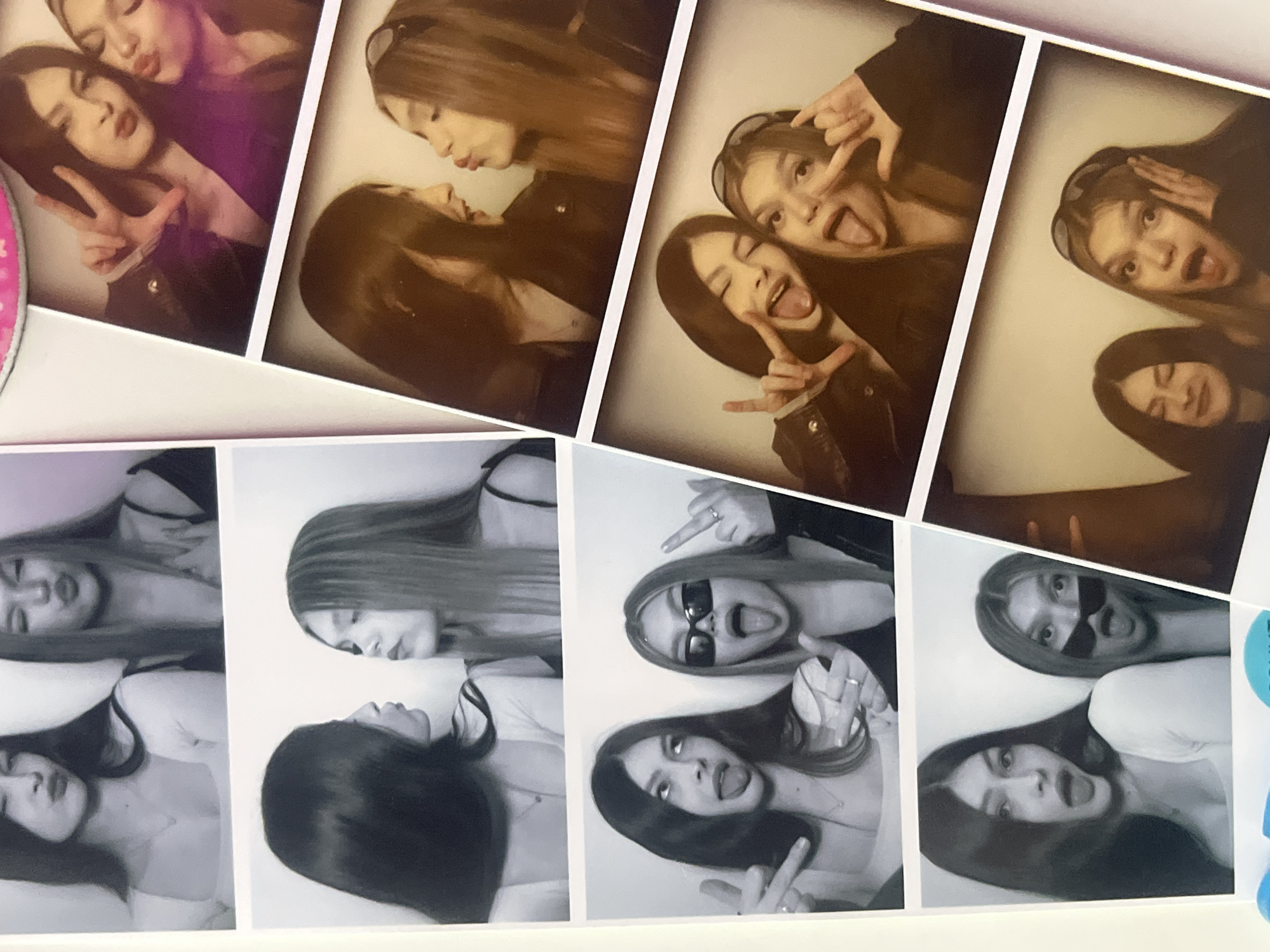 This media file presents a collection of photobooth strips, likely physical prints, laid out on a white surface, possibly a table or background. The strips are arranged in an overlapping, dynamic manner, with some showing color (predominantly sepia tones with one vibrant purple background frame) and others in grayscale.
The subjects are two young women with long, dark hair, appearing in various poses across all the frames. In many shots, they are seen together, while some strips feature individual close-ups. Their attire includes dark jackets (possibly leather), a purple top, and a white top, with one woman wearing sunglasses in some grayscale frames. Rings are visible on their fingers in several shots.
The activity taking place is typical of a photobooth session: the women are posing playfully, displaying a range of joyful and silly expressions. These include smiling, laughing, pouting with "kiss" faces, sticking out their tongues, and making hand gestures such as peace signs and "rock on" symbols. Some frames show them looking at each other, while others have them looking directly at the camera. The general emotion conveyed is one of happiness and camaraderie.
The setting for the individual photos is a generic photobooth with plain backgrounds. The overall image captures these strips as physical objects. There are no discernible time-of-day or weather cues within the photobooth images themselves. The provided location context is Saint Petersburg, Russia, though there are no explicit visual cues within the image to confirm this specific location. No readable text is visible on the photobooth strips or the surrounding surface.